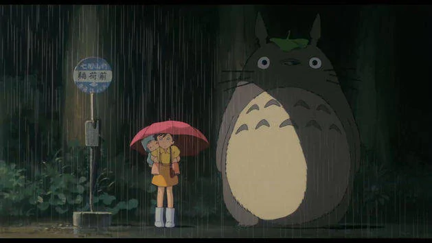 Satsuki, Mei, and Totoro waiting at a bus stop in My Neighbor Totoro