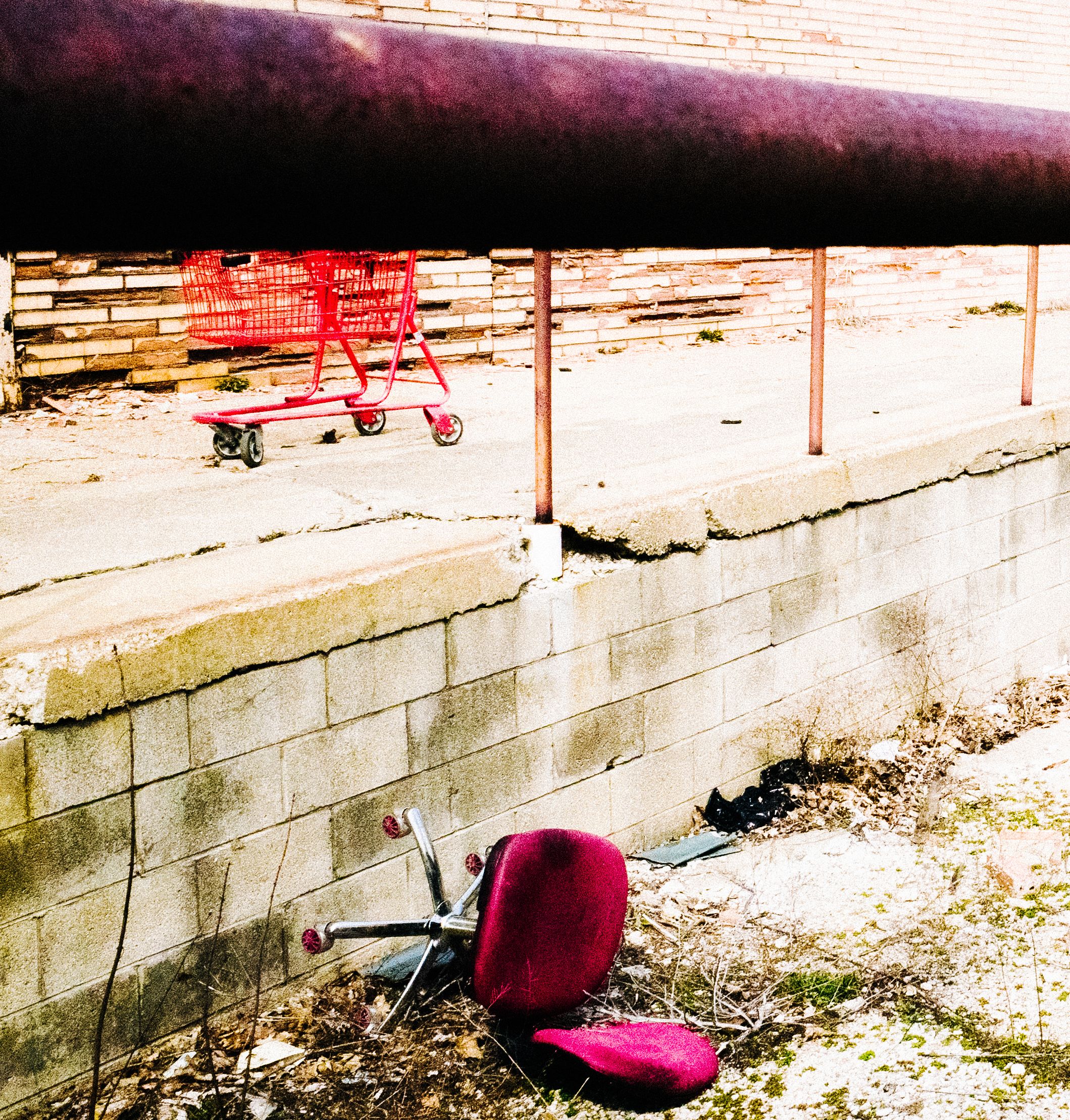 An overturned purple office chair and red shopping cart in a deserted parking lot
