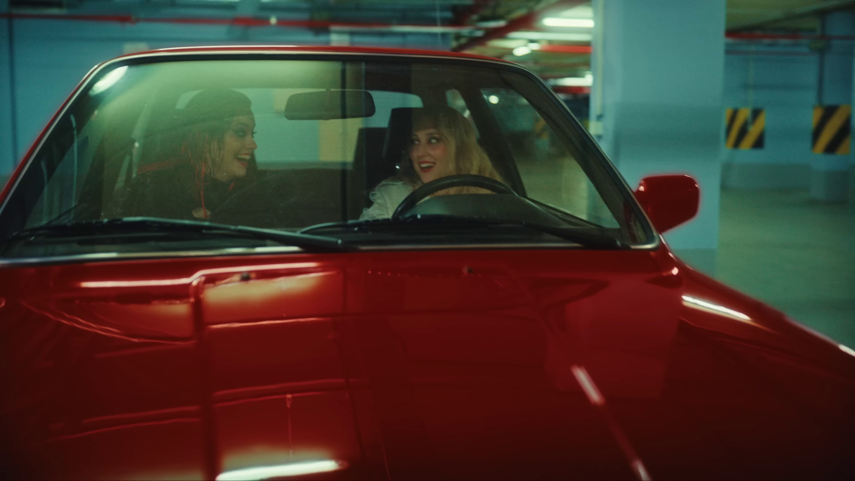 image of Salena seated behind the wheel of a red convertible with Teya next to her