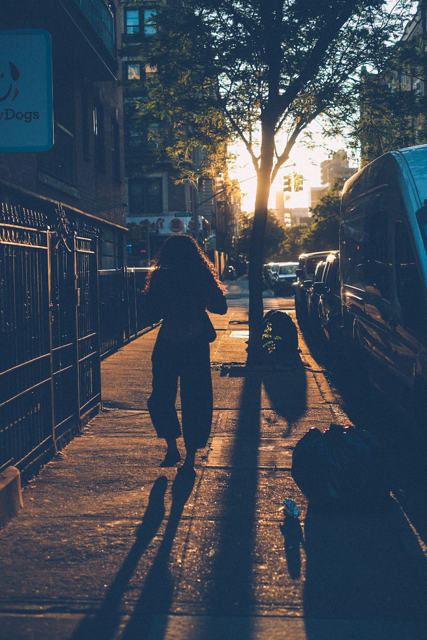A woman walks down a city street at sunset, silhouetted by sun rays.