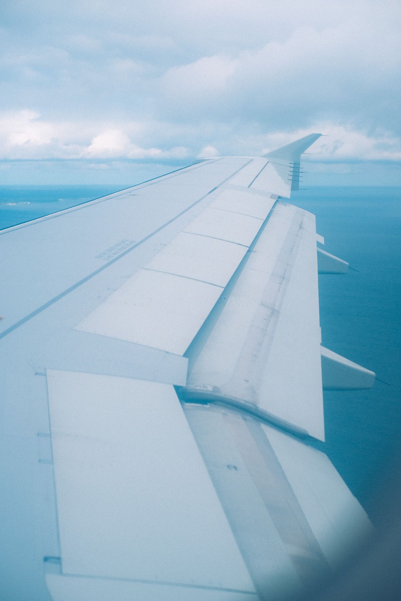 A view of an airplane wing, blue tinted, overlooking land and sea.