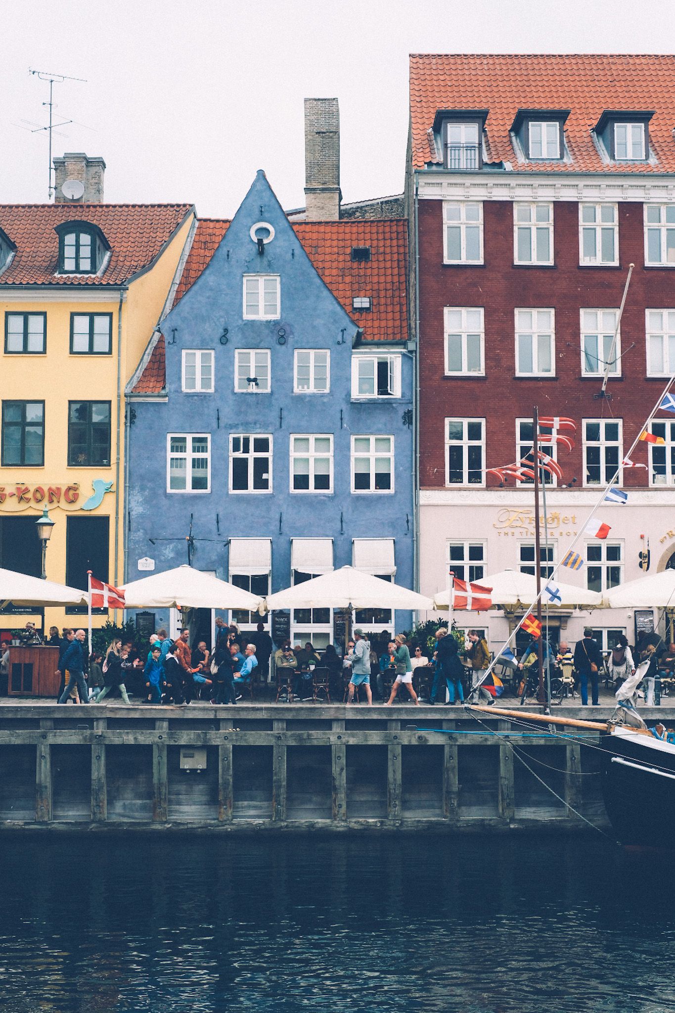 A yellow, blue, and red building sit on the harbor in Nyhaven, Copenhagen, crowds passing in front of them.