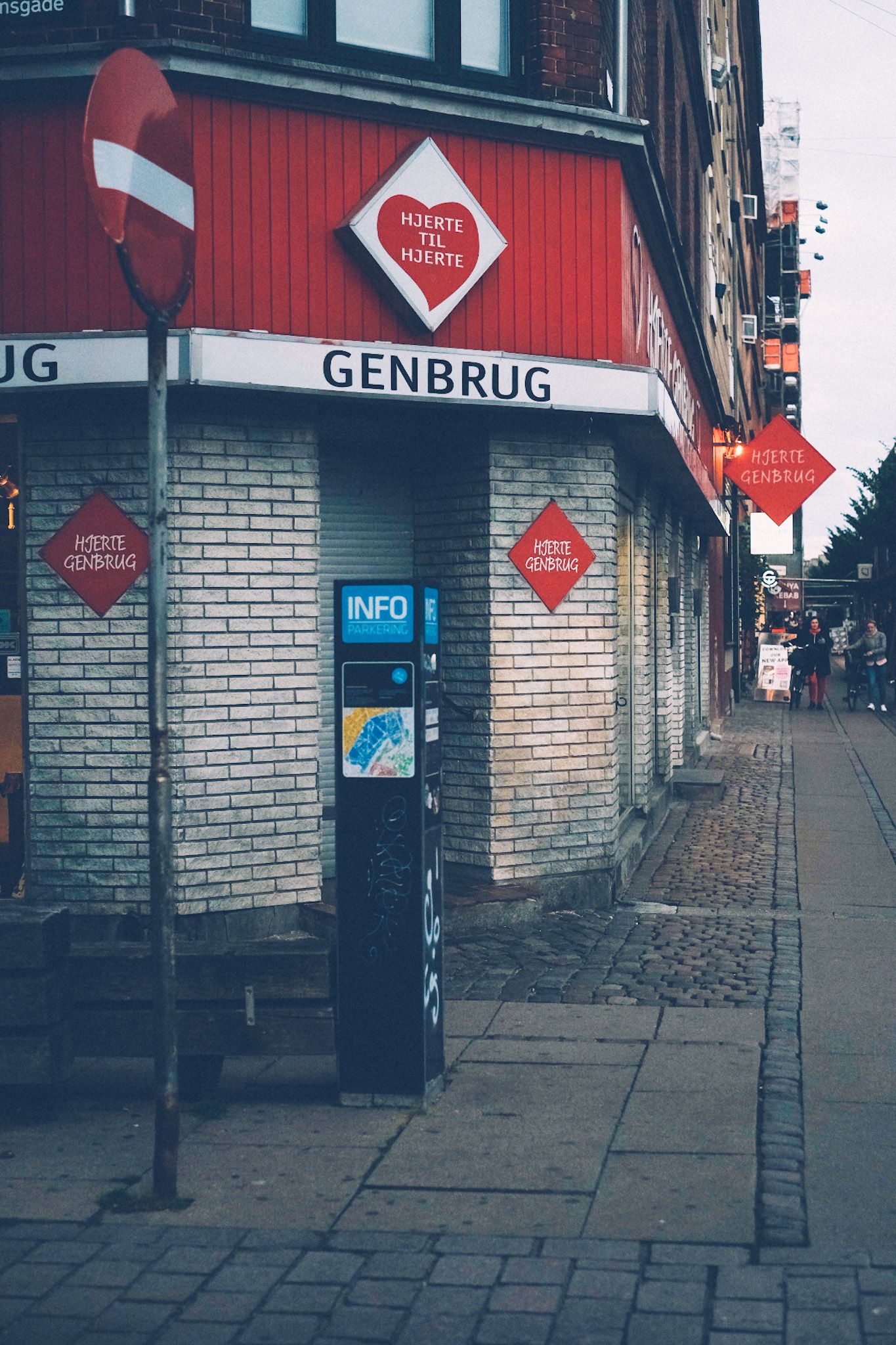 On a street corner of Copenhagen, a corner store with red branding has white letters displaying “Genbrug”.