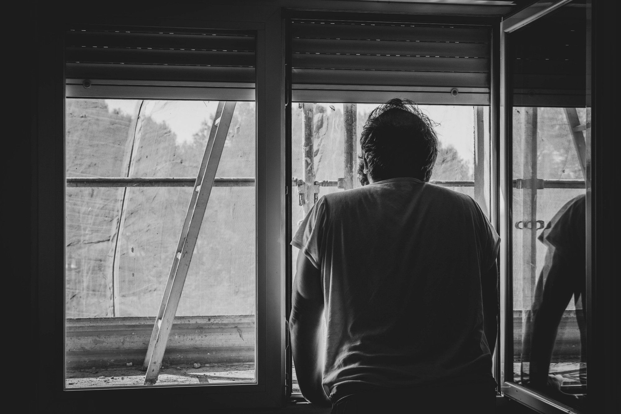 Man standing at a window. Seemingly lost in thought. In B&W.