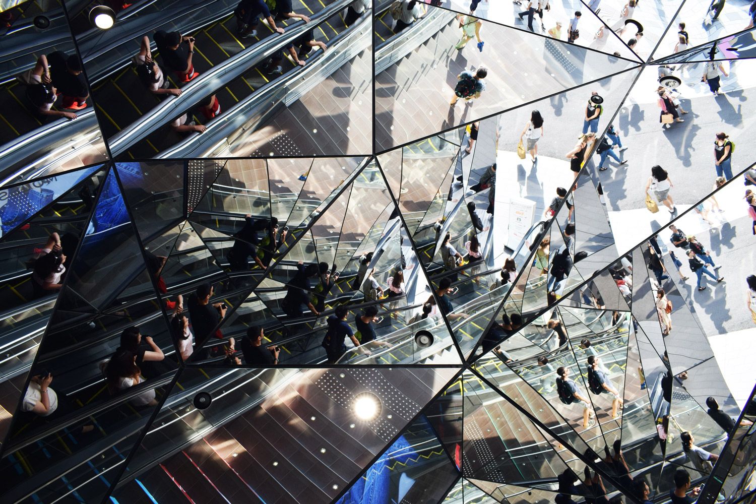 Kaleidoscopic view of people riding an escalator and exiting into a concrete plaza.