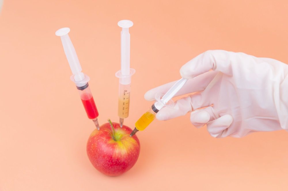 Apple with syringes sticking into in on an orange background.