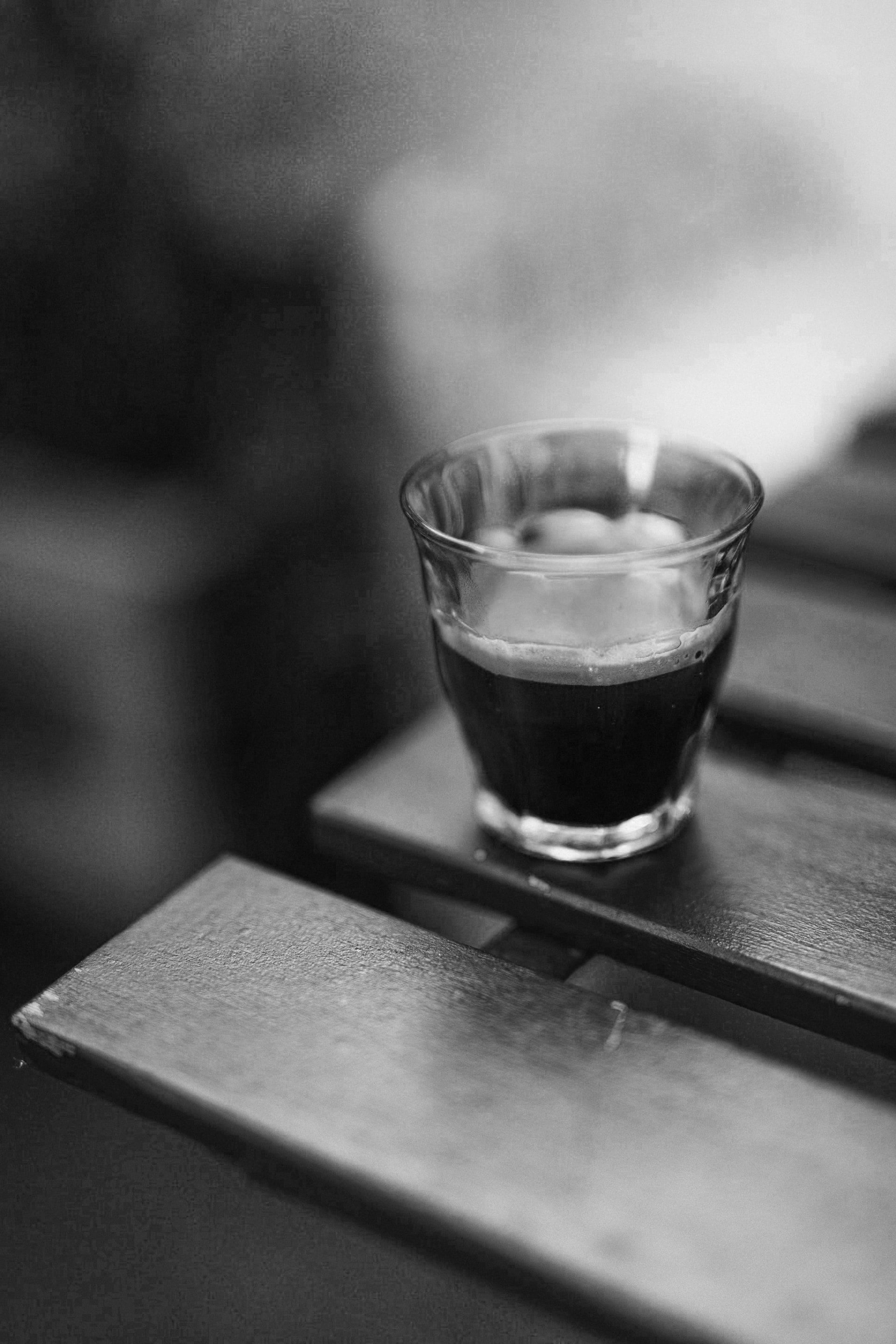 A shot of espresso in a glass on the edge of a wooden table