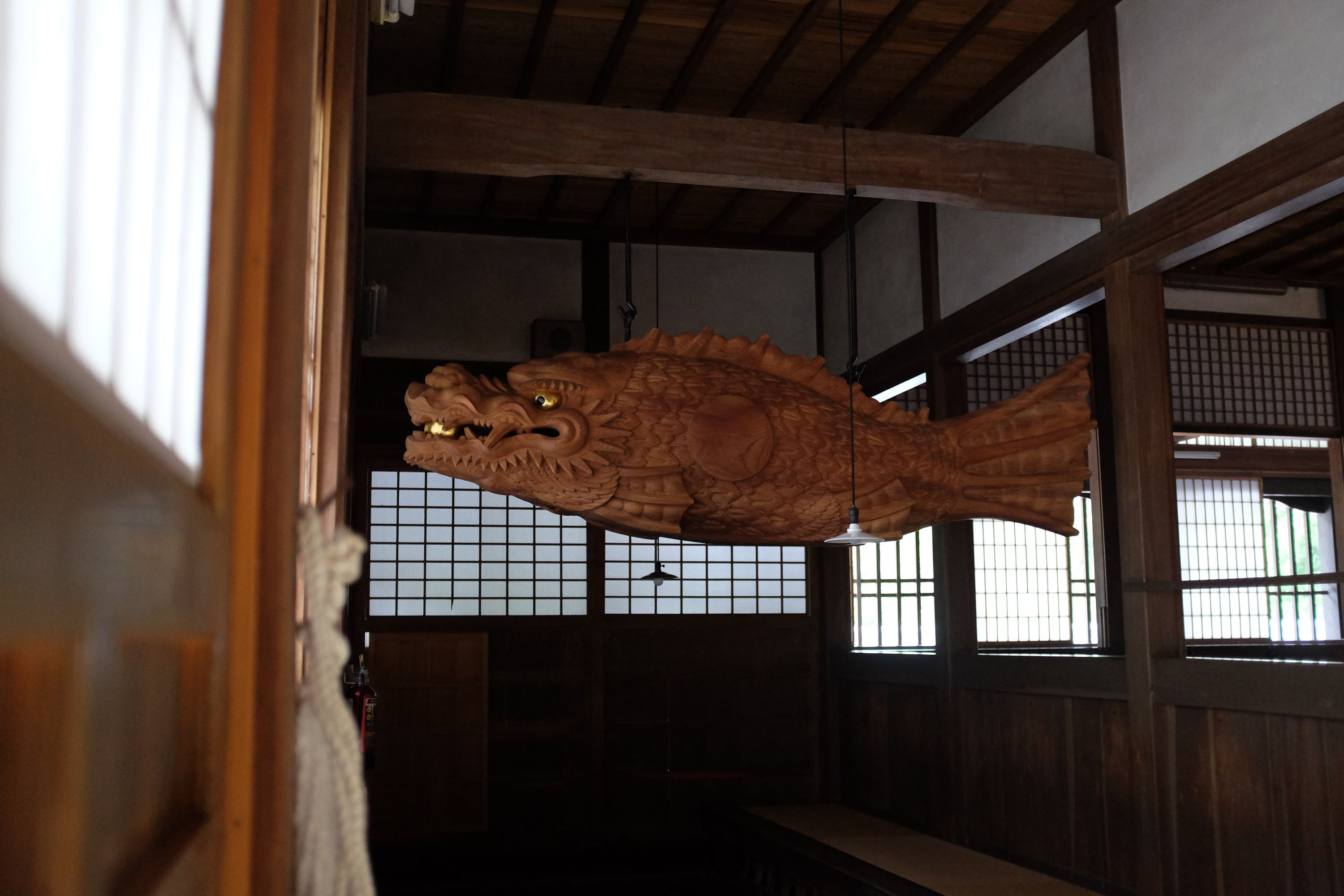 A menacing looking carved wooden fish-monster hangs from the ceiling of a Japanese temple.