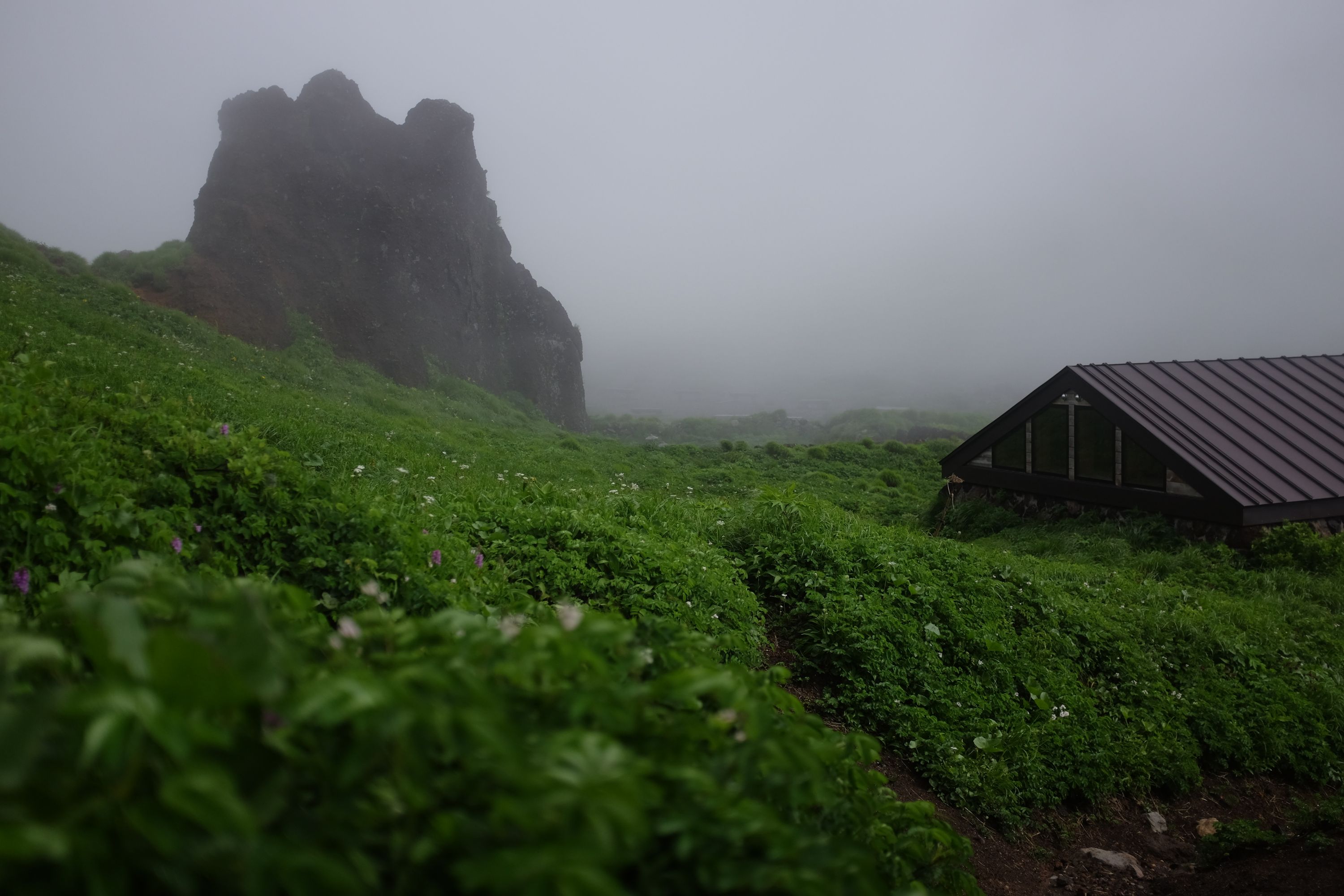 A mountain hut by an enormous black rock inside a foggy crater.