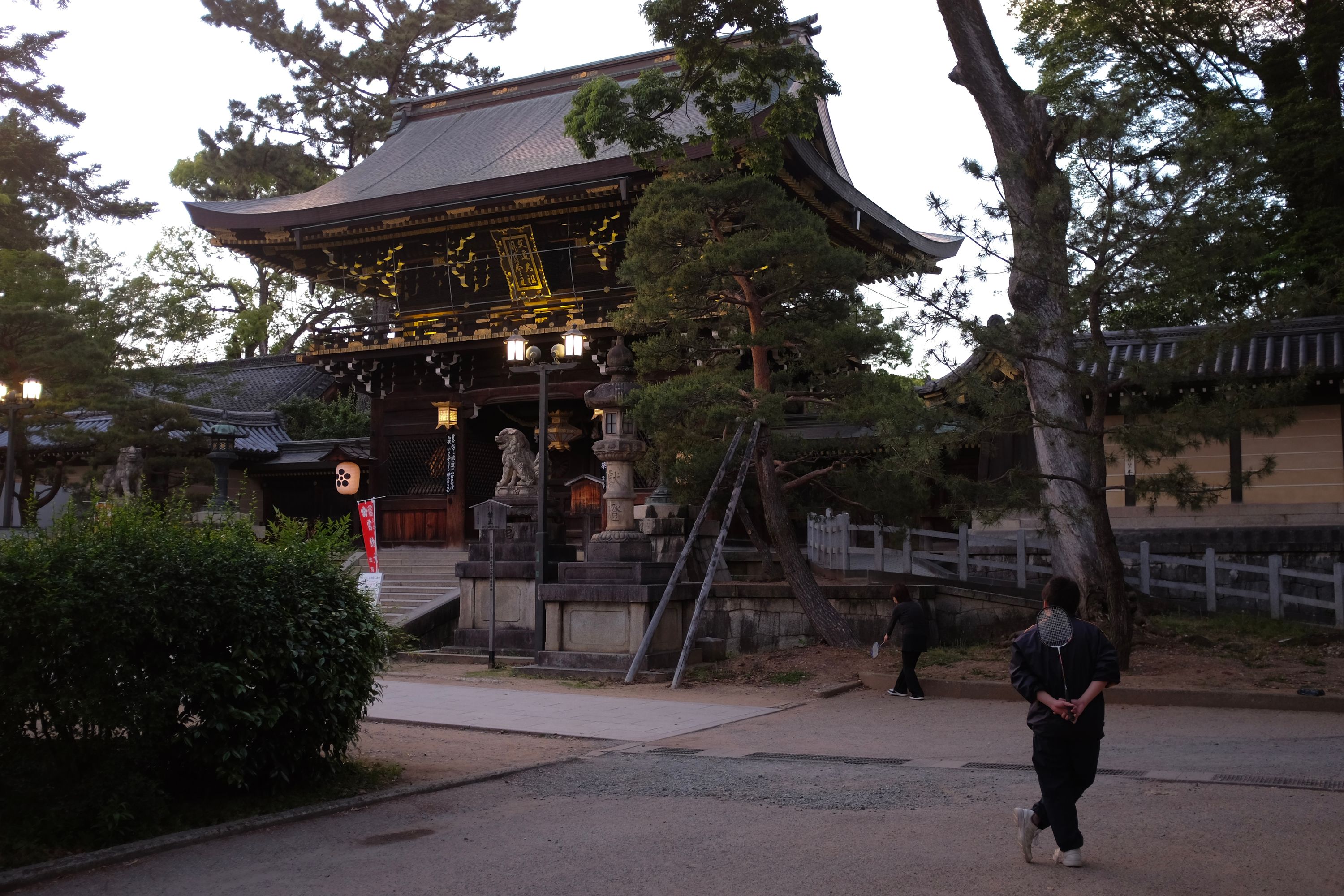 Two people play badminton in the garden of a Japanese shrine.