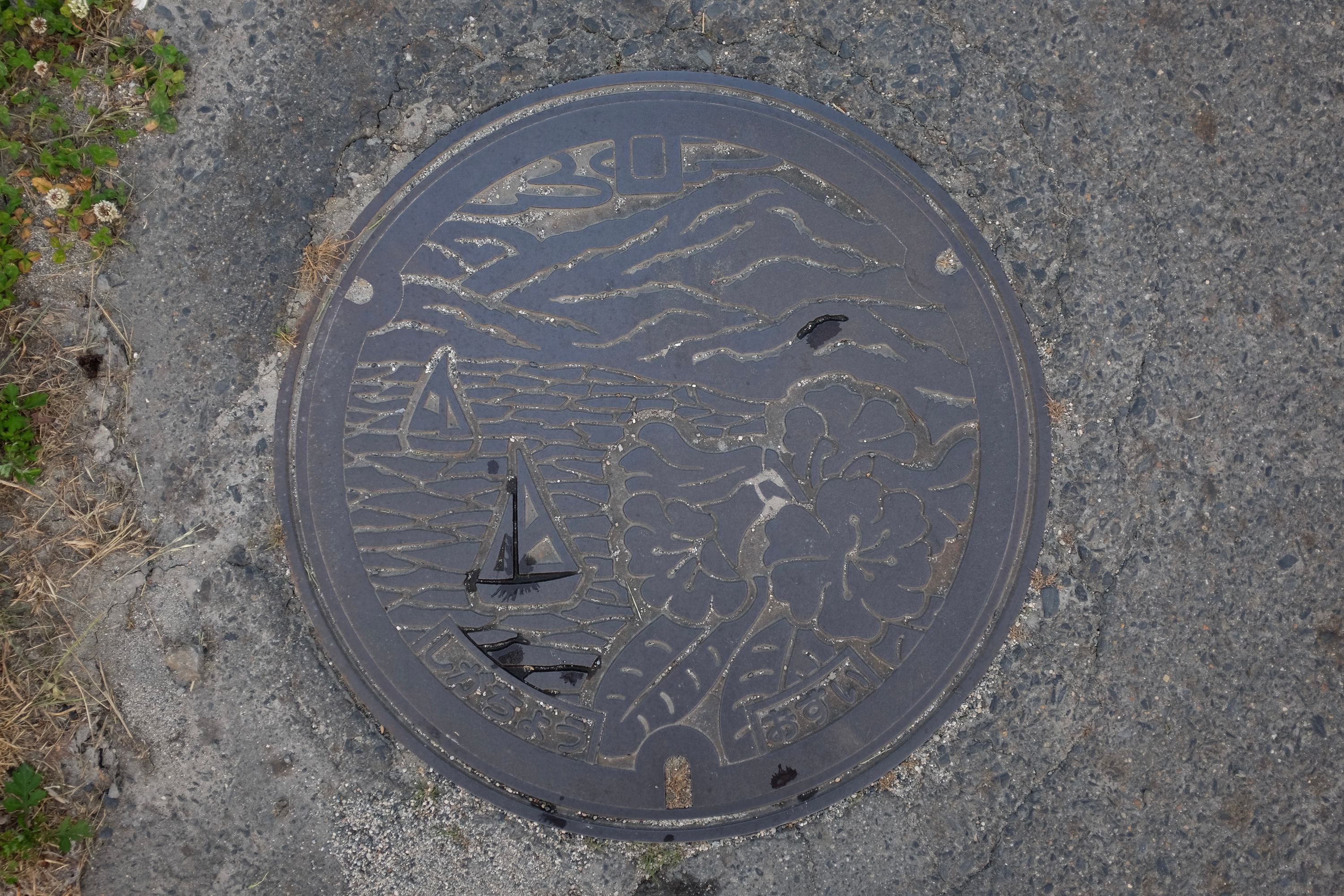 Manhole cover with picture of sailboats on a lake.