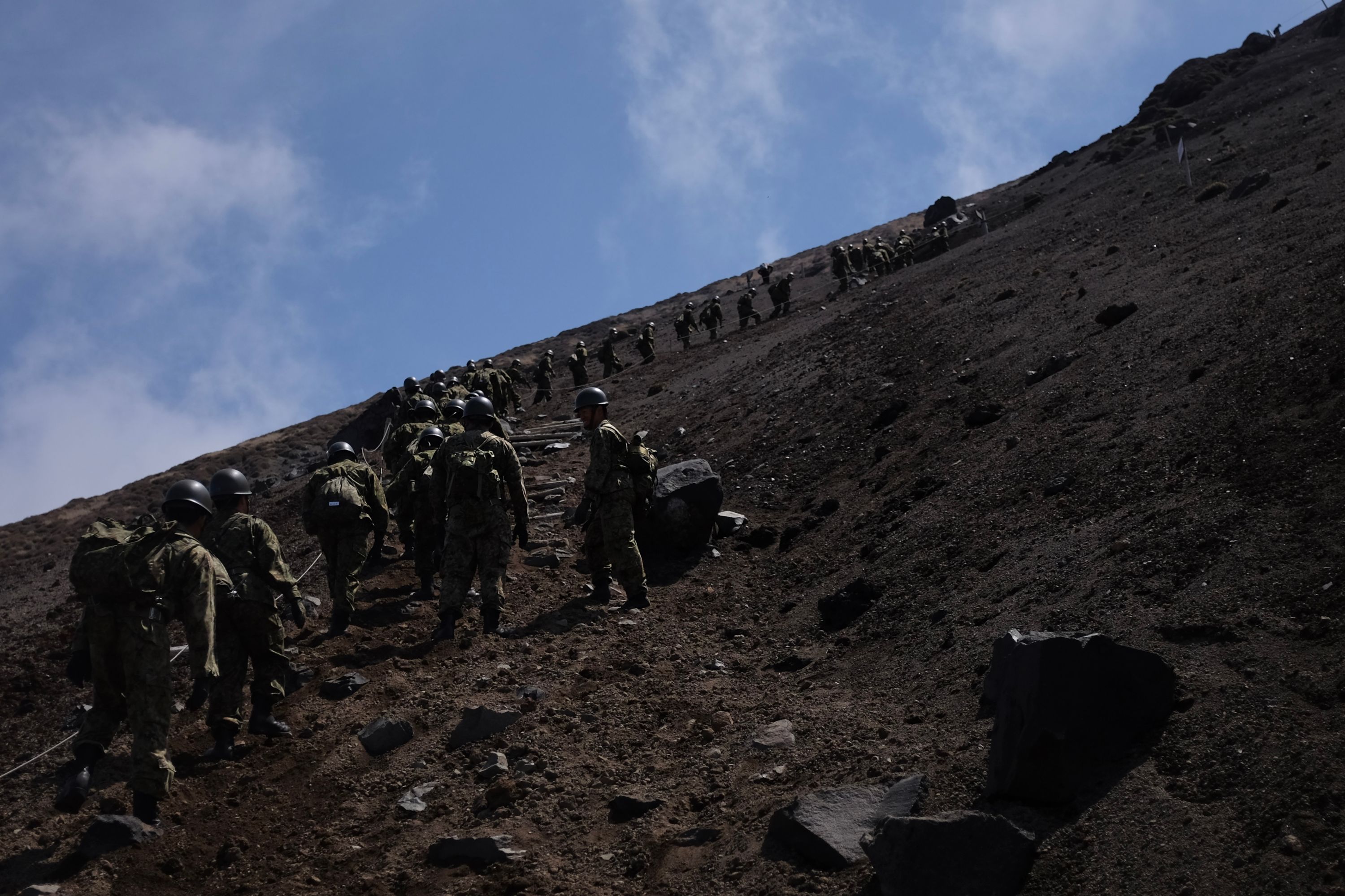 The soldiers march away from the camera, up the mountain.