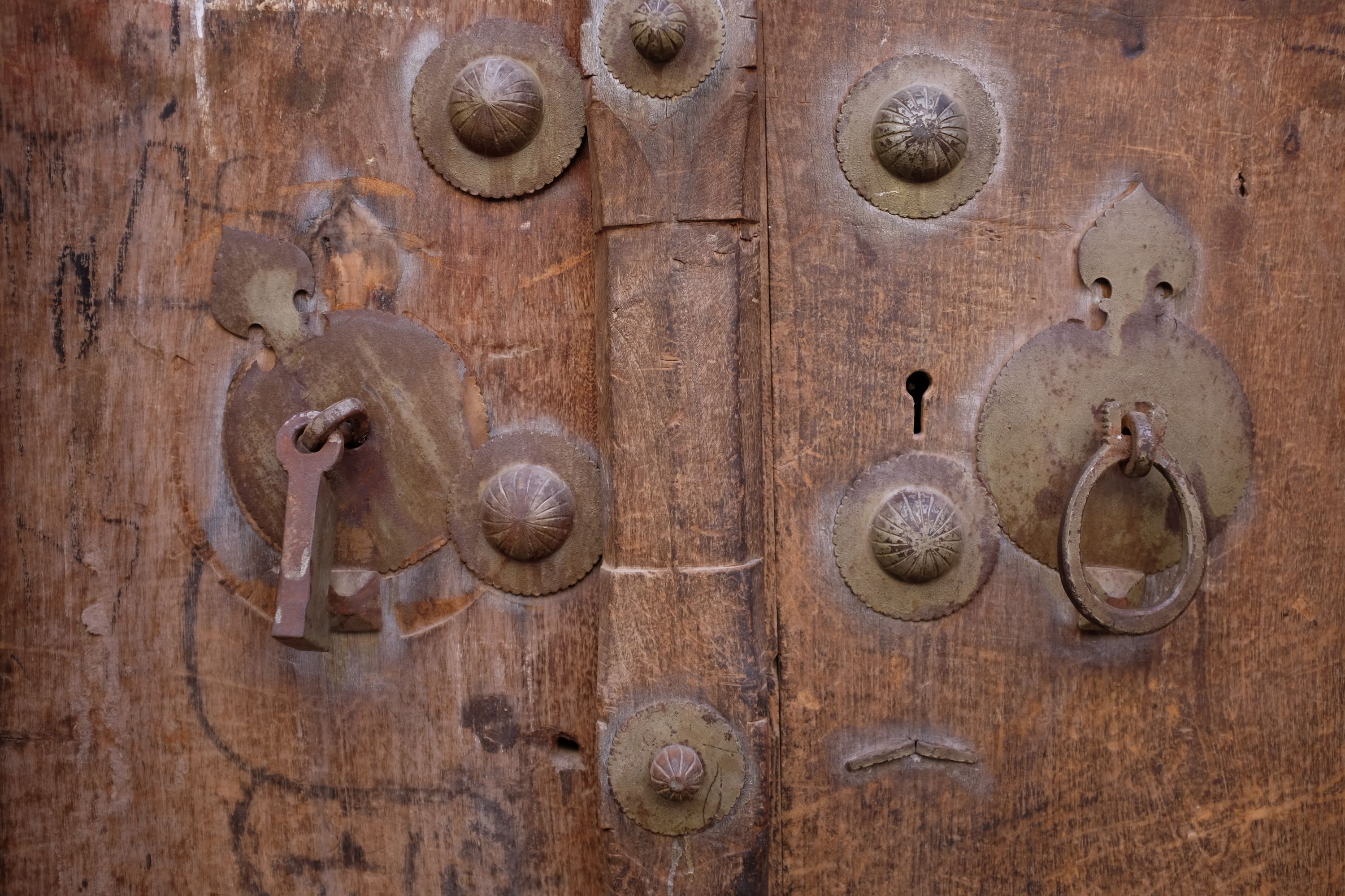 A straight and a circular door knocker on a door that looks very old.