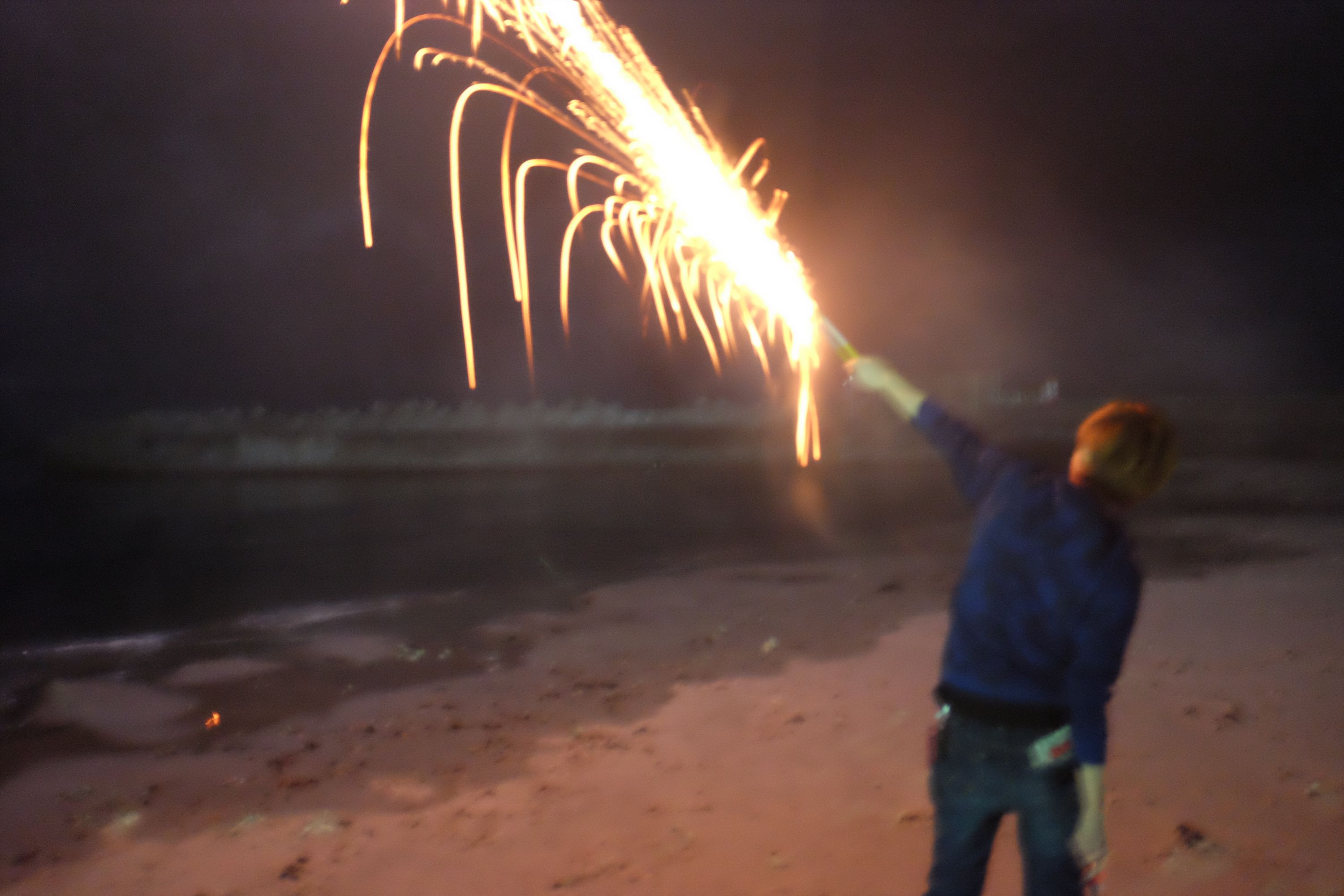 A boy shoots a firecracker on a beach.