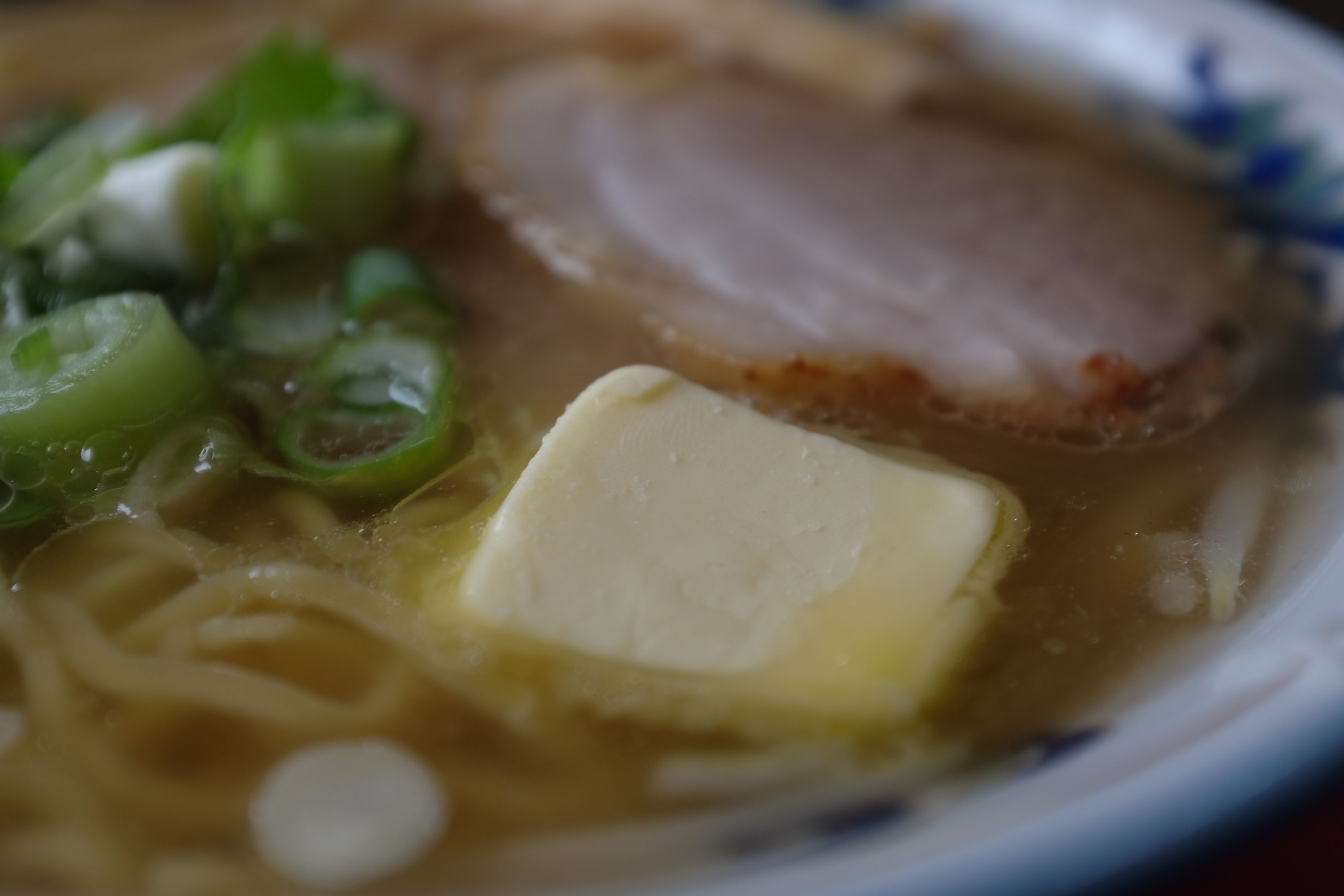 Closeup of a bowl of ramen with a piece of butter showing a human fingerprint in the broth.