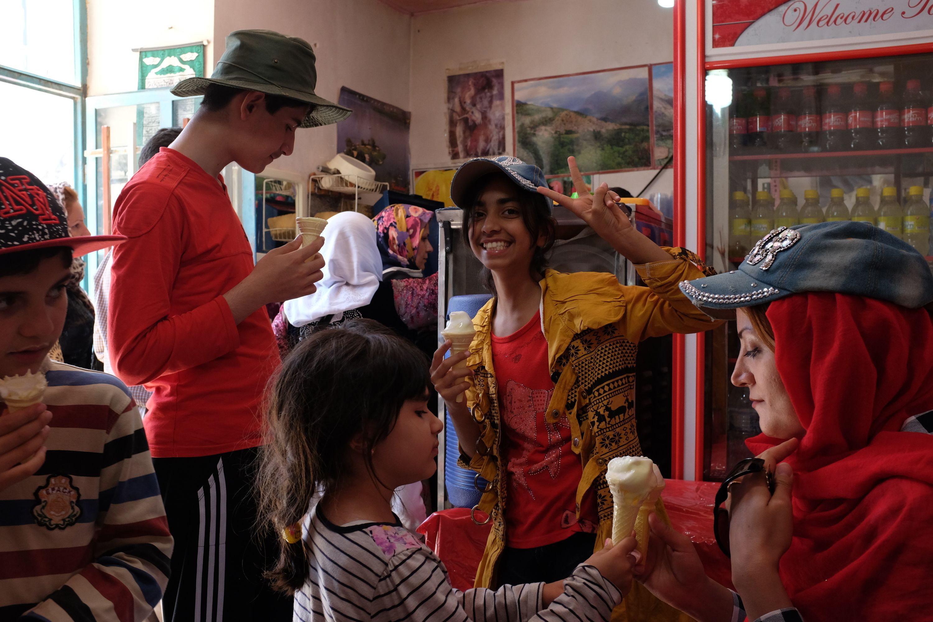 Three girls and two boys of various ages eat ice cream in a shop; one of the girls shows the V-sign into the camera.