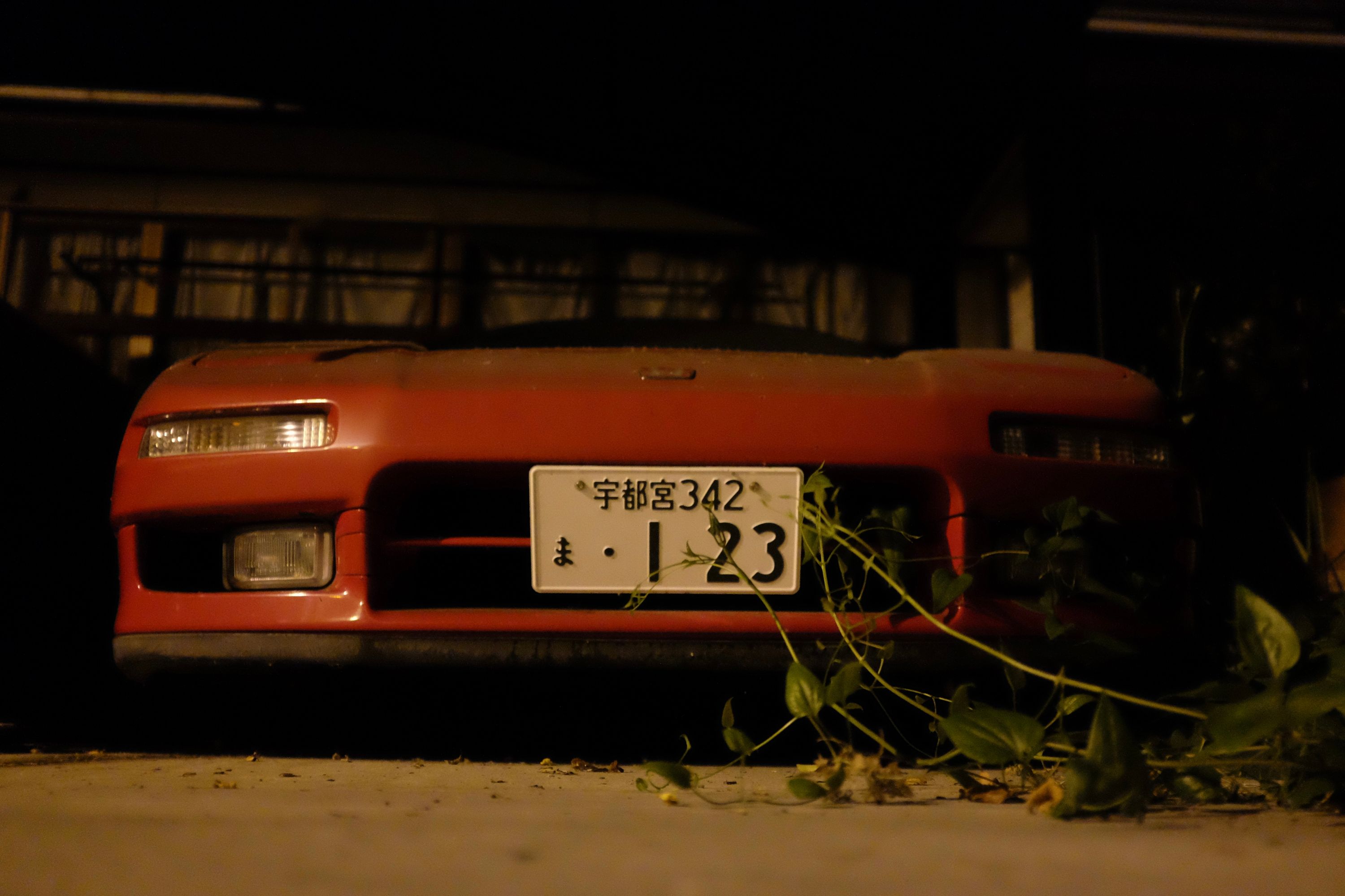 A NSX, very dusty and partly overgrown with weeds, stands in a garage at night.