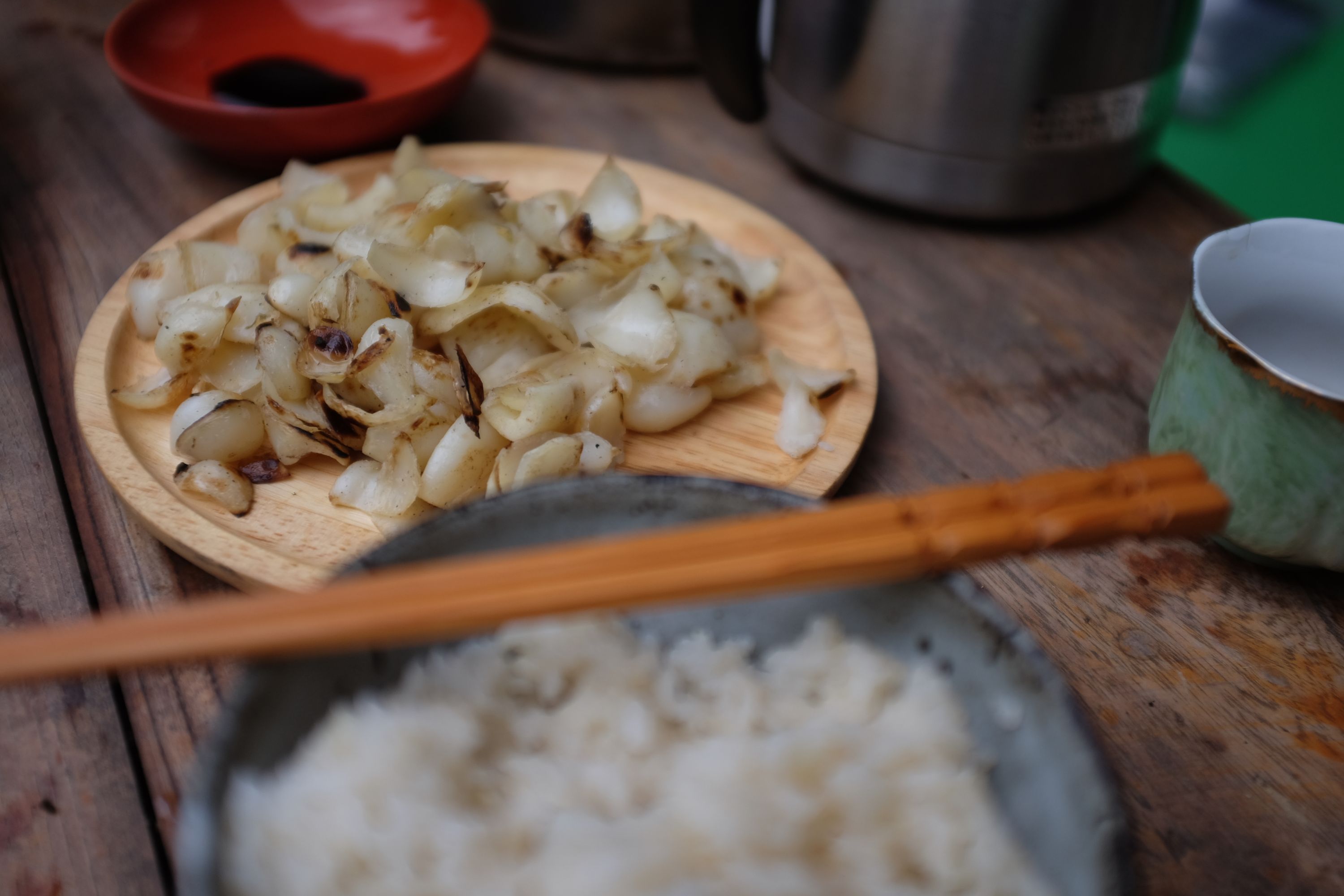 A plate of fried lily bulbs, a bowl of rice, and a pair of chopstcks on a breakfast table.