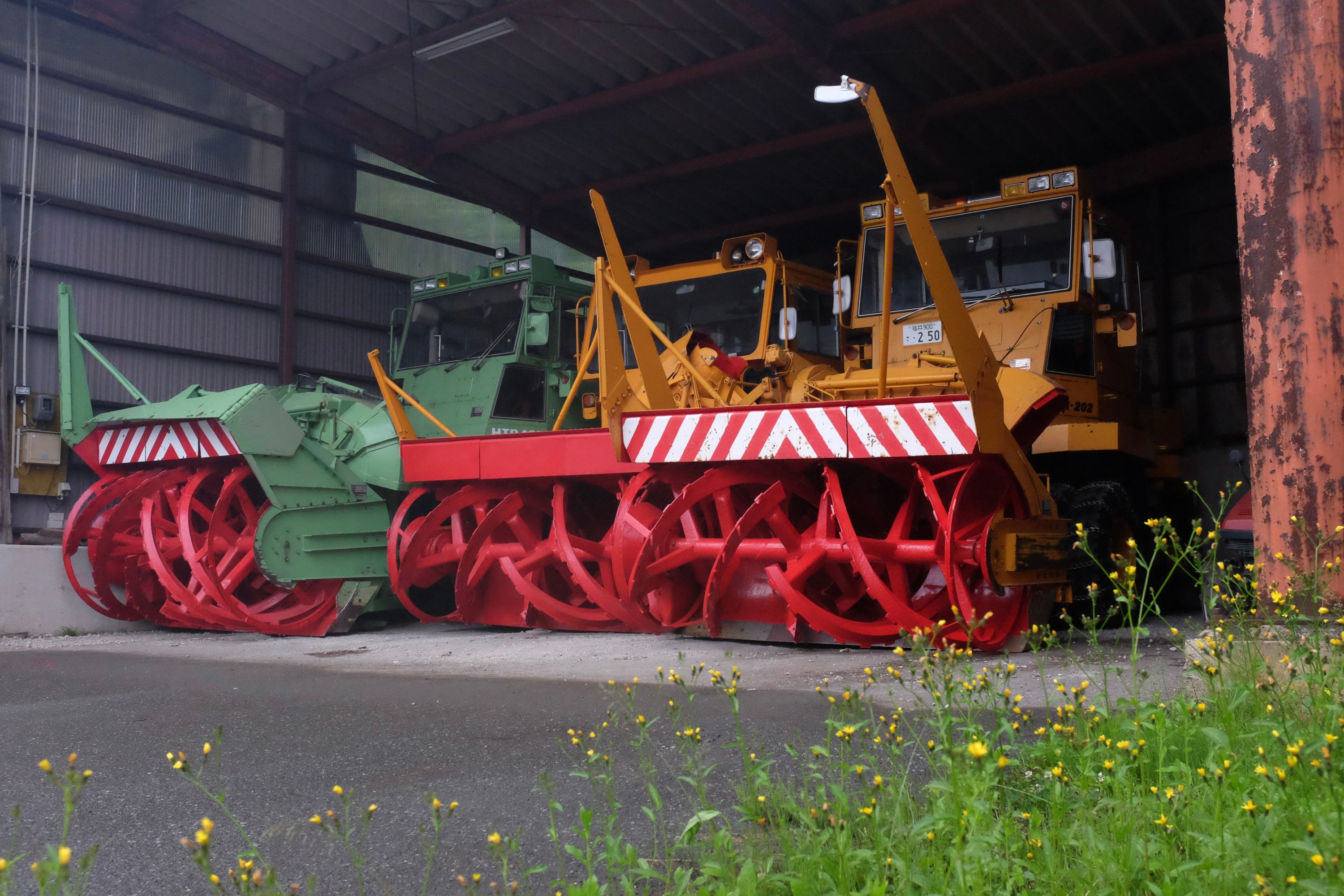 Green and yellow snowplows in an open garage.