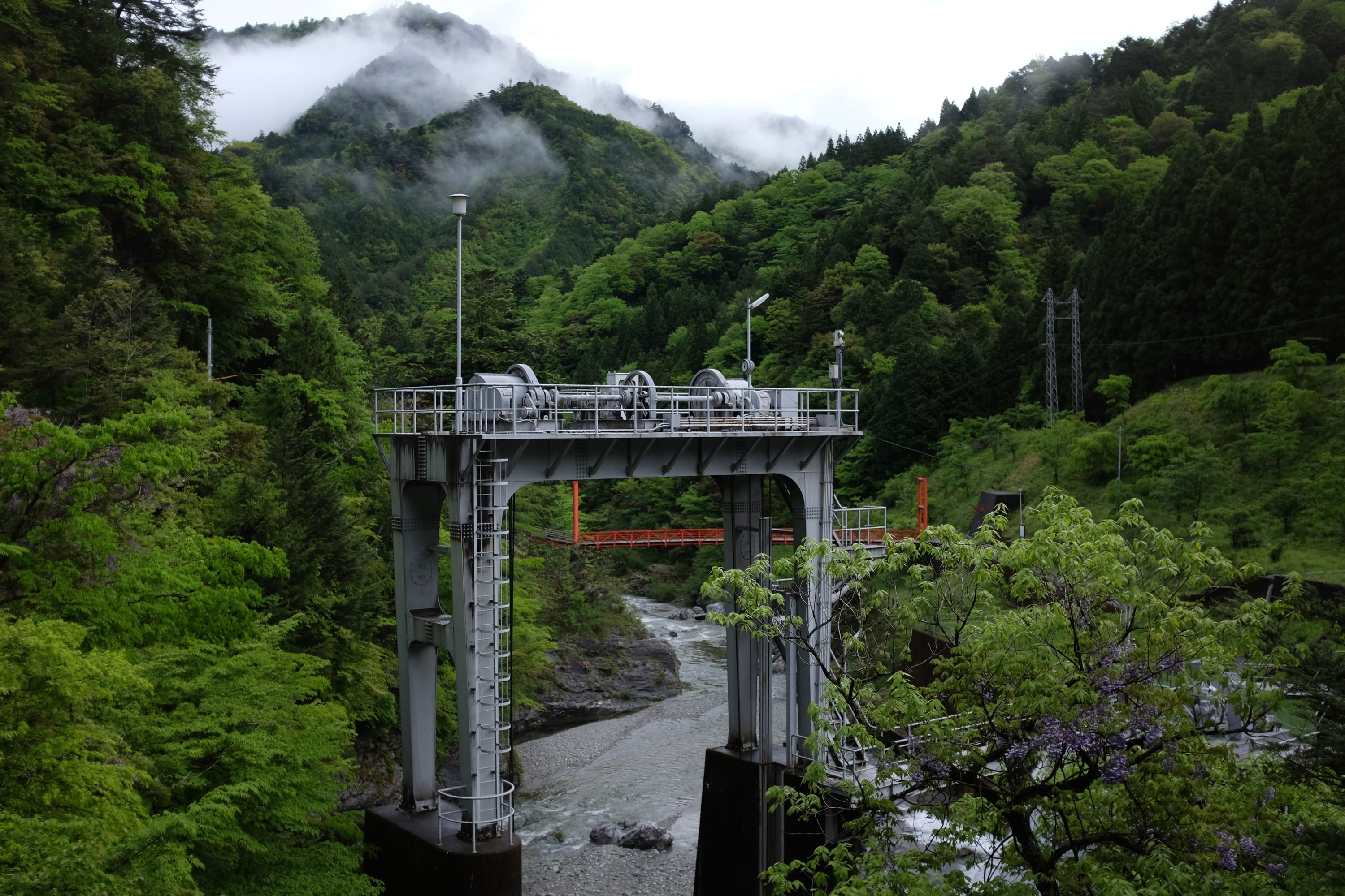 The machinery of a hydroelectric power station stands in thickly forested, verdant green hills.