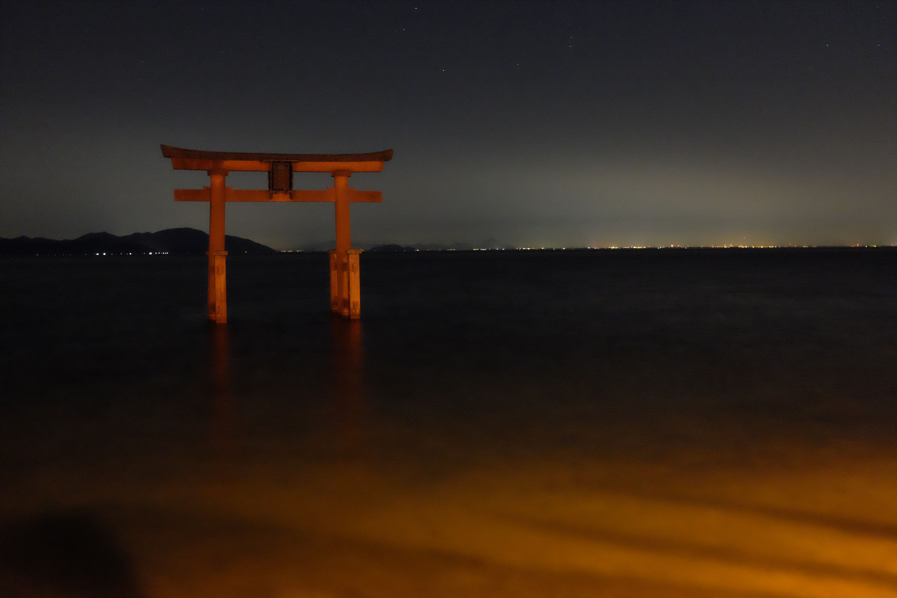 The red torii gate of a Japanese shrine stands in the waters of a lake at night.