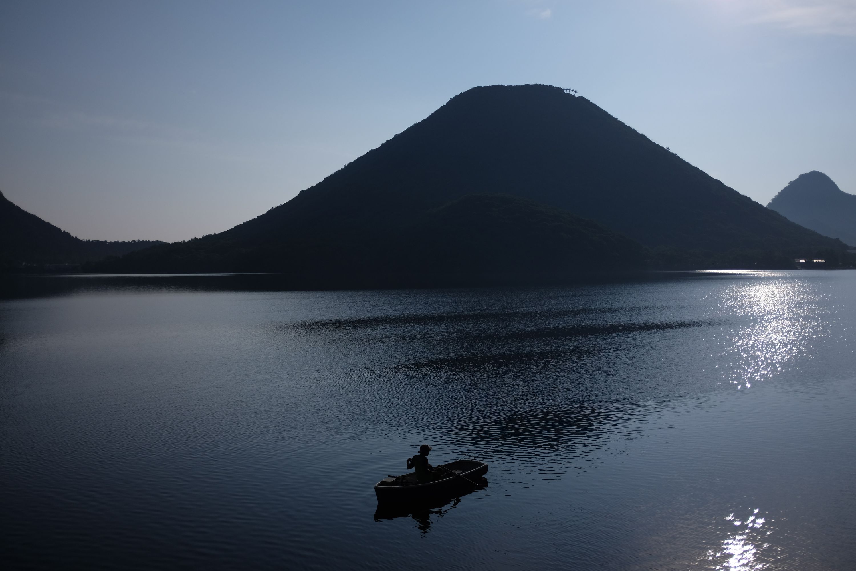 A man rows a boat on a lake in front of a perfect volcanic cone, Mount Haruna.