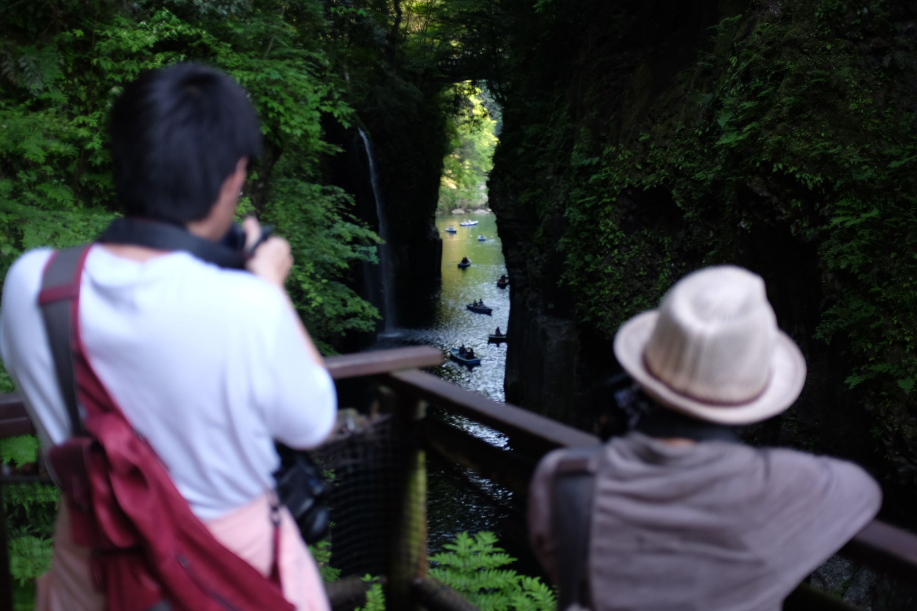 Two people taking photos of several such sightseeing boats from a vantage point above the gorge.