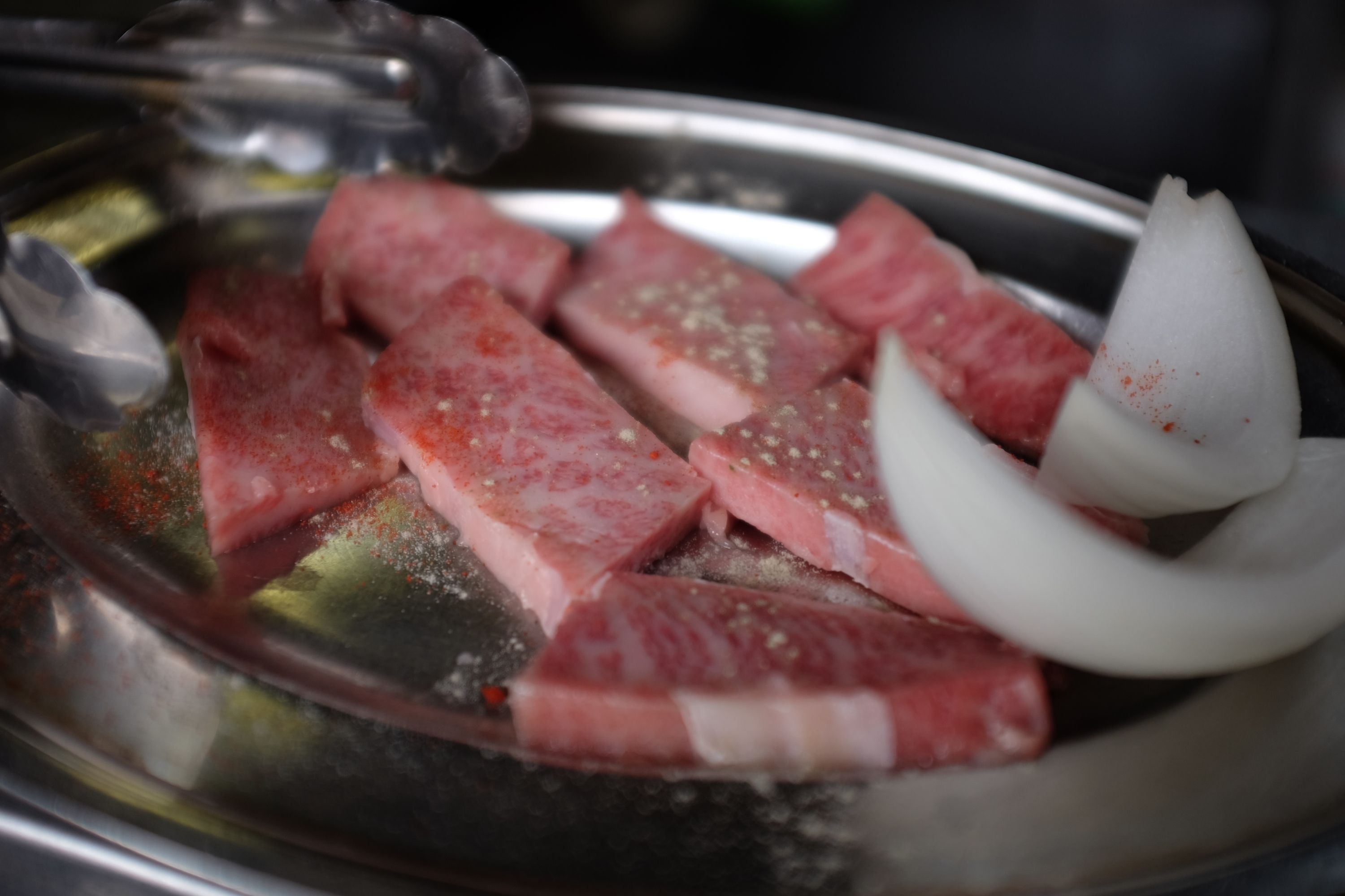 Closeup of raw pieces of fatty Kōbe beef and slices of onion.