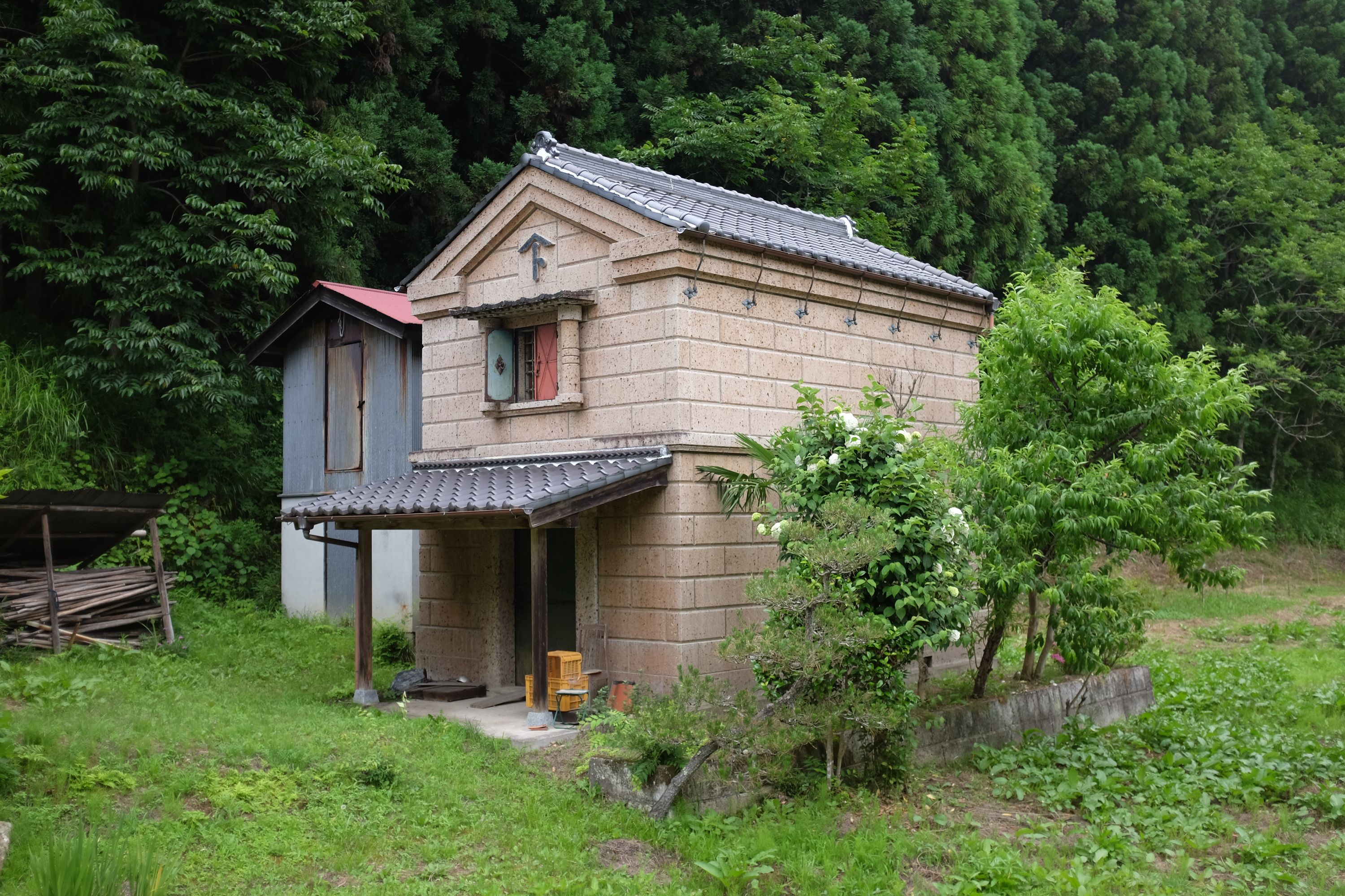 A kura, a Japanese storehouse, stand by a forested hillside.