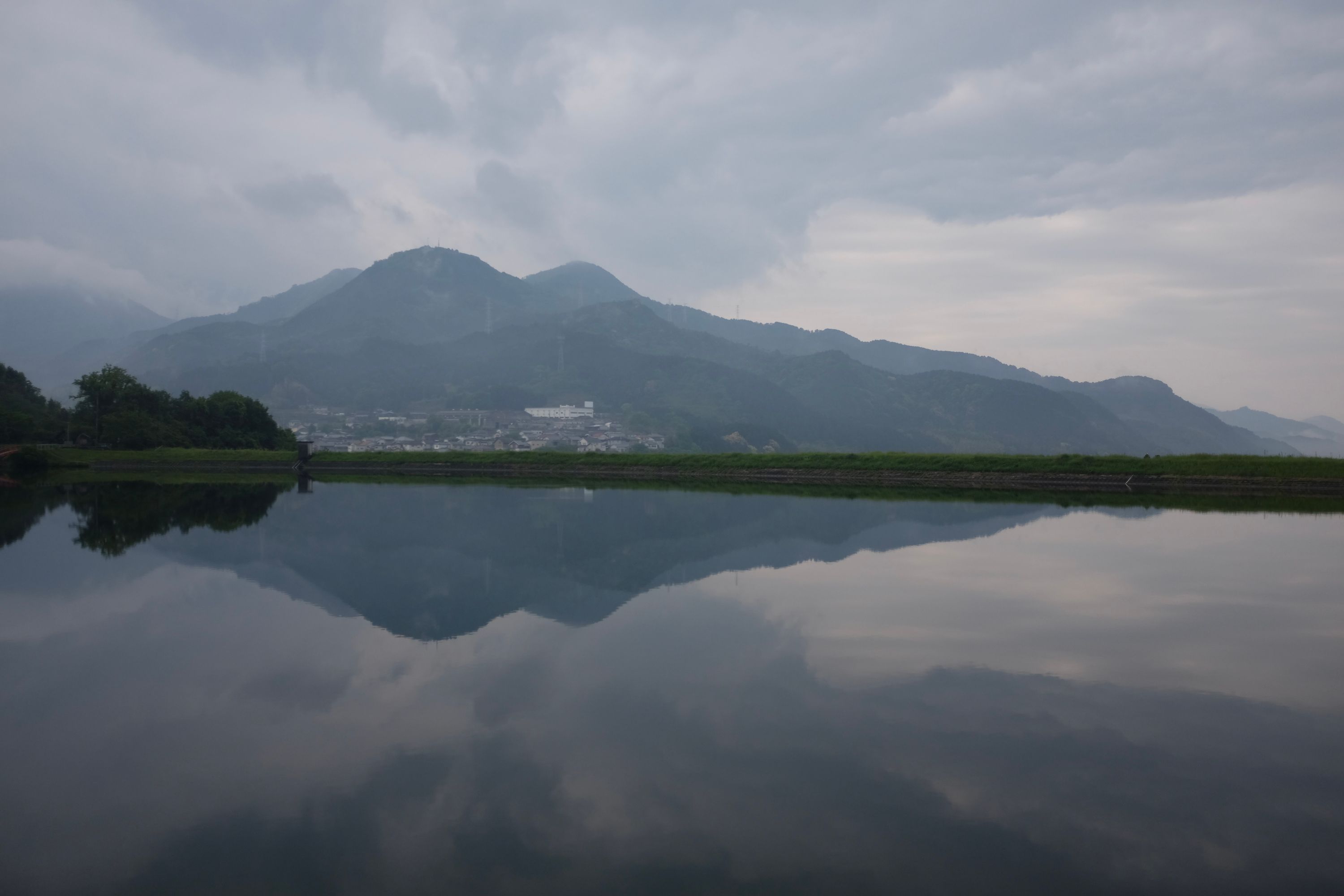 Mountains reflected in a flooded rice field under a cloudy sky.