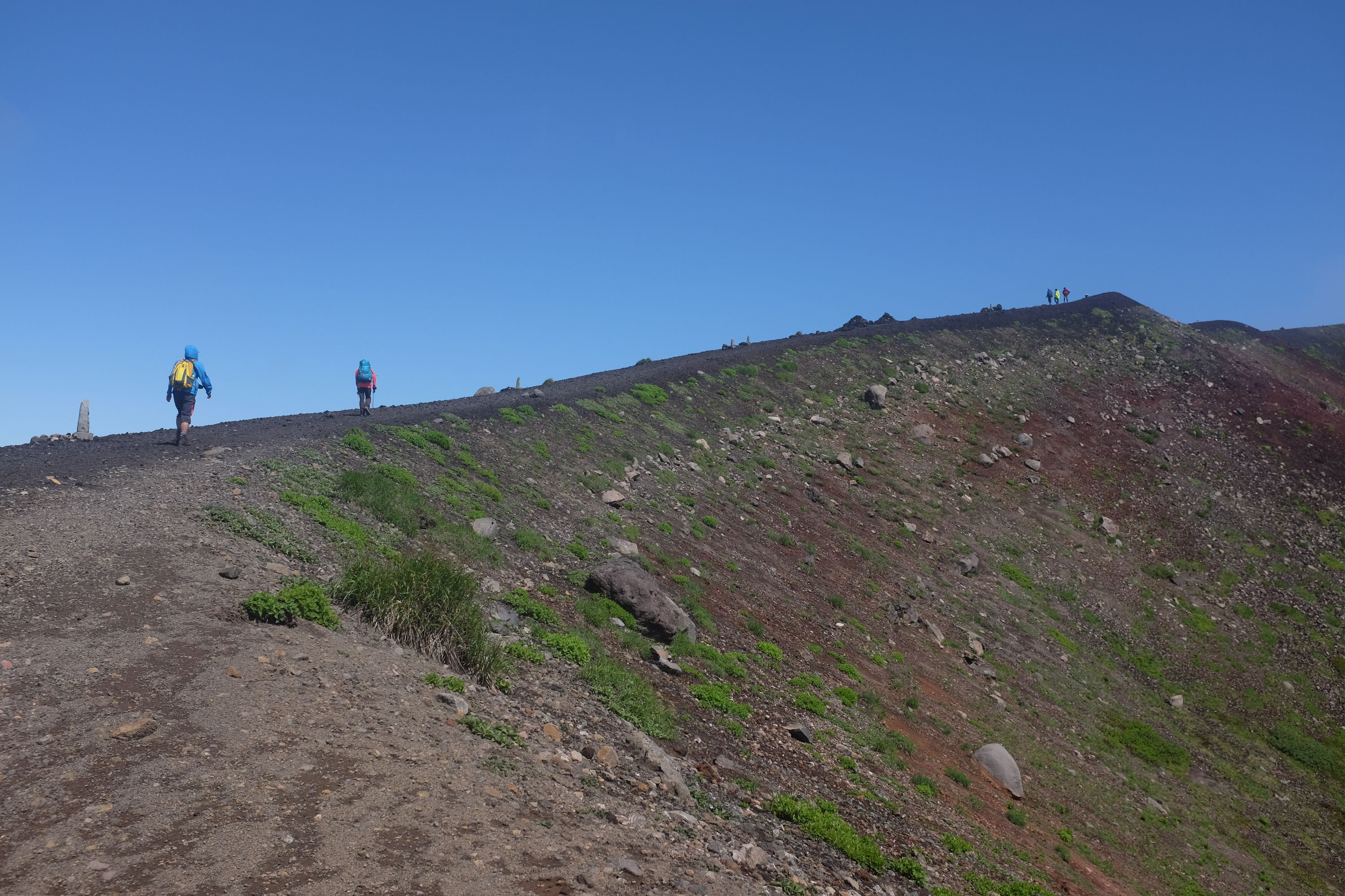 A couple of climbers walk on the rim of a volcanic crater.