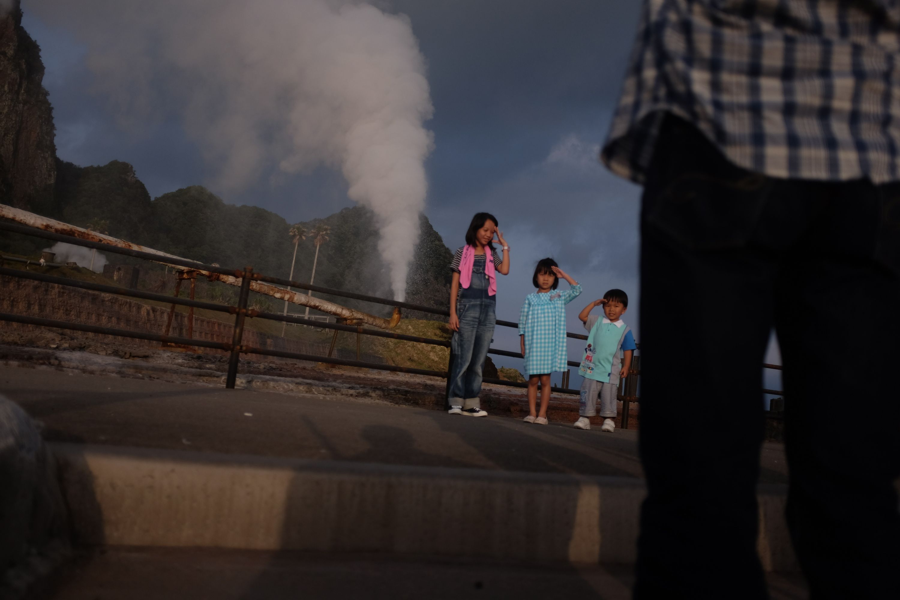 Children pose in front of a small geyser of hot water.