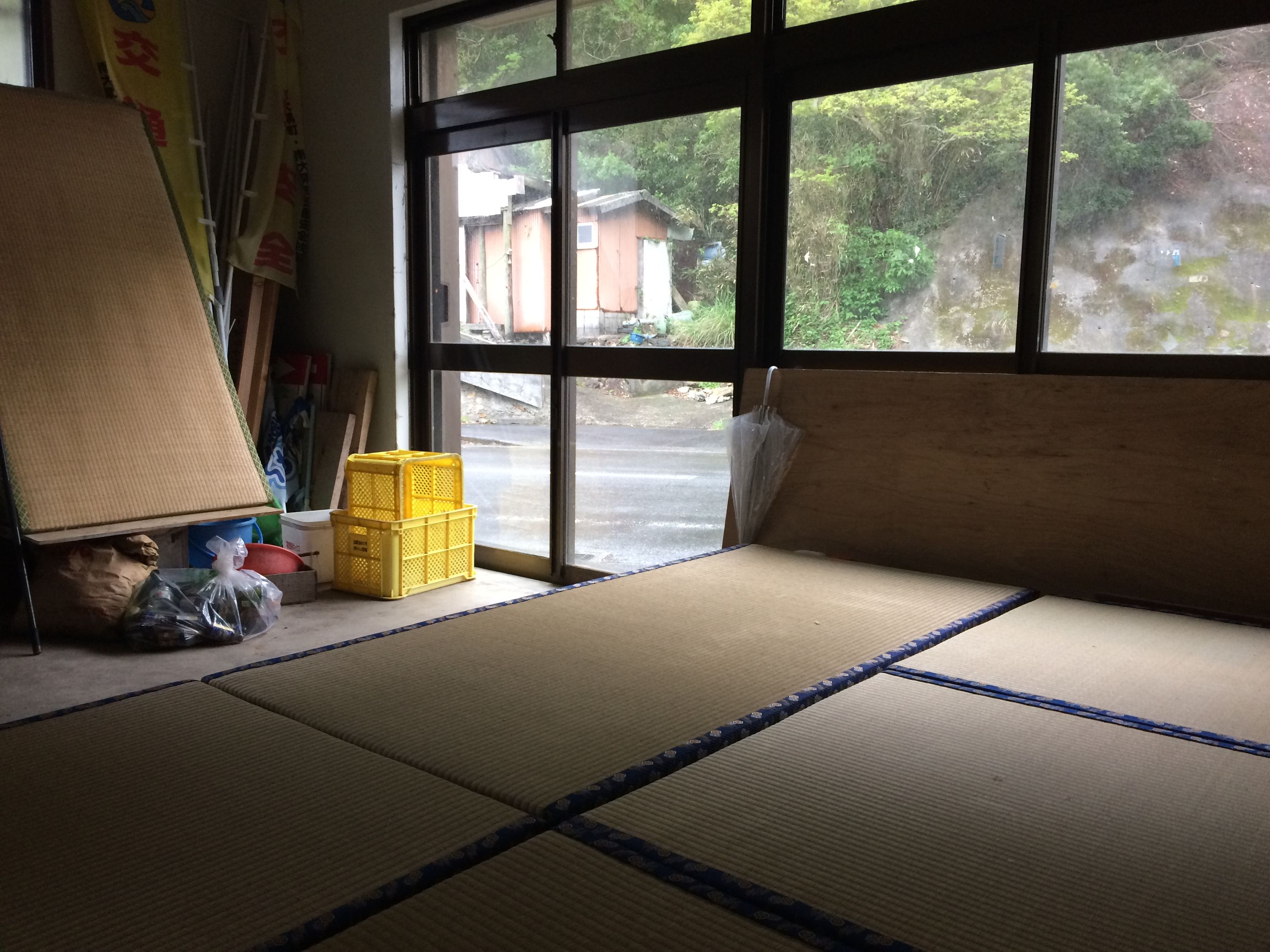 Tatami mats in a small house whose windows look out on a village street, it’s raining outside.