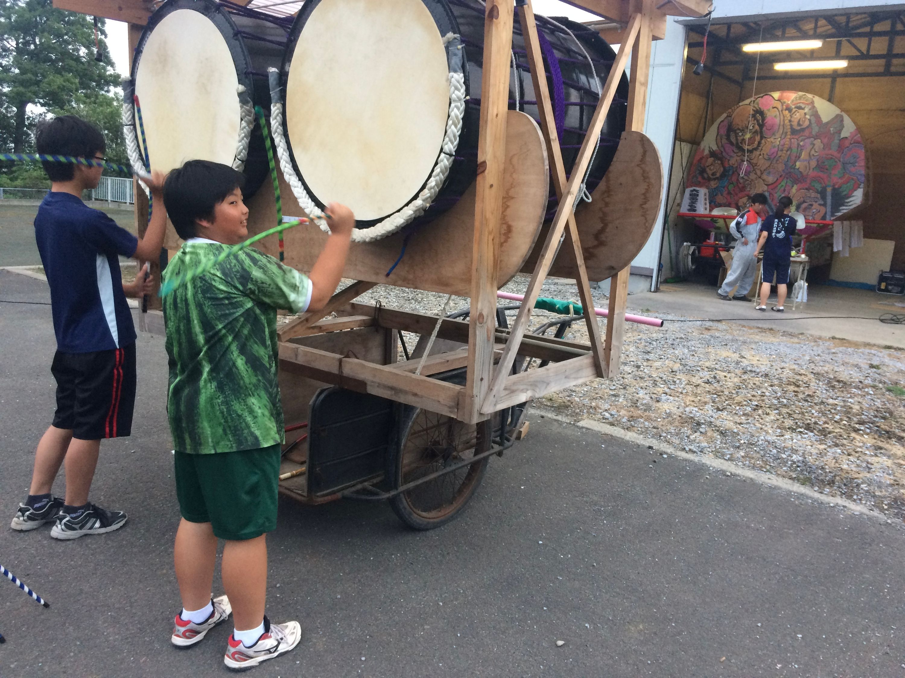Two boys, one of them dressed — and shaped — like a watermelon, play a pair of large drums.