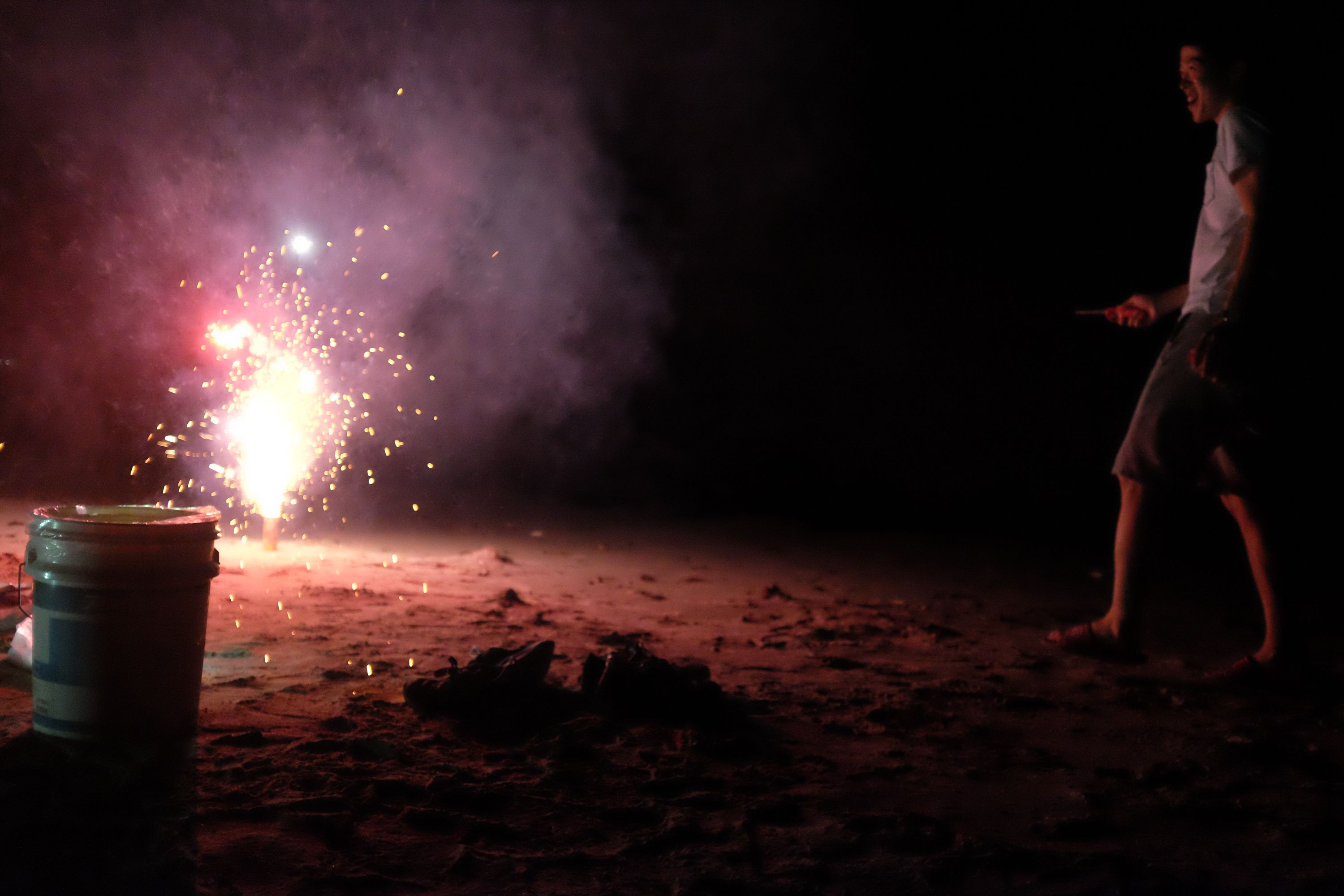 A boy shoots fireworks on the beach.