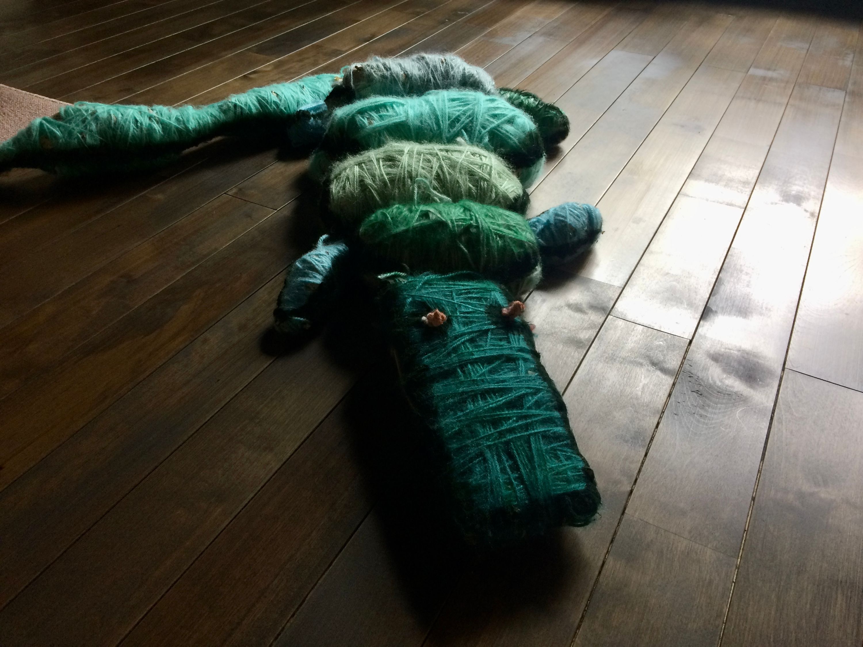 An alligator made of yarns of green wool rests on a polished wooden floor.