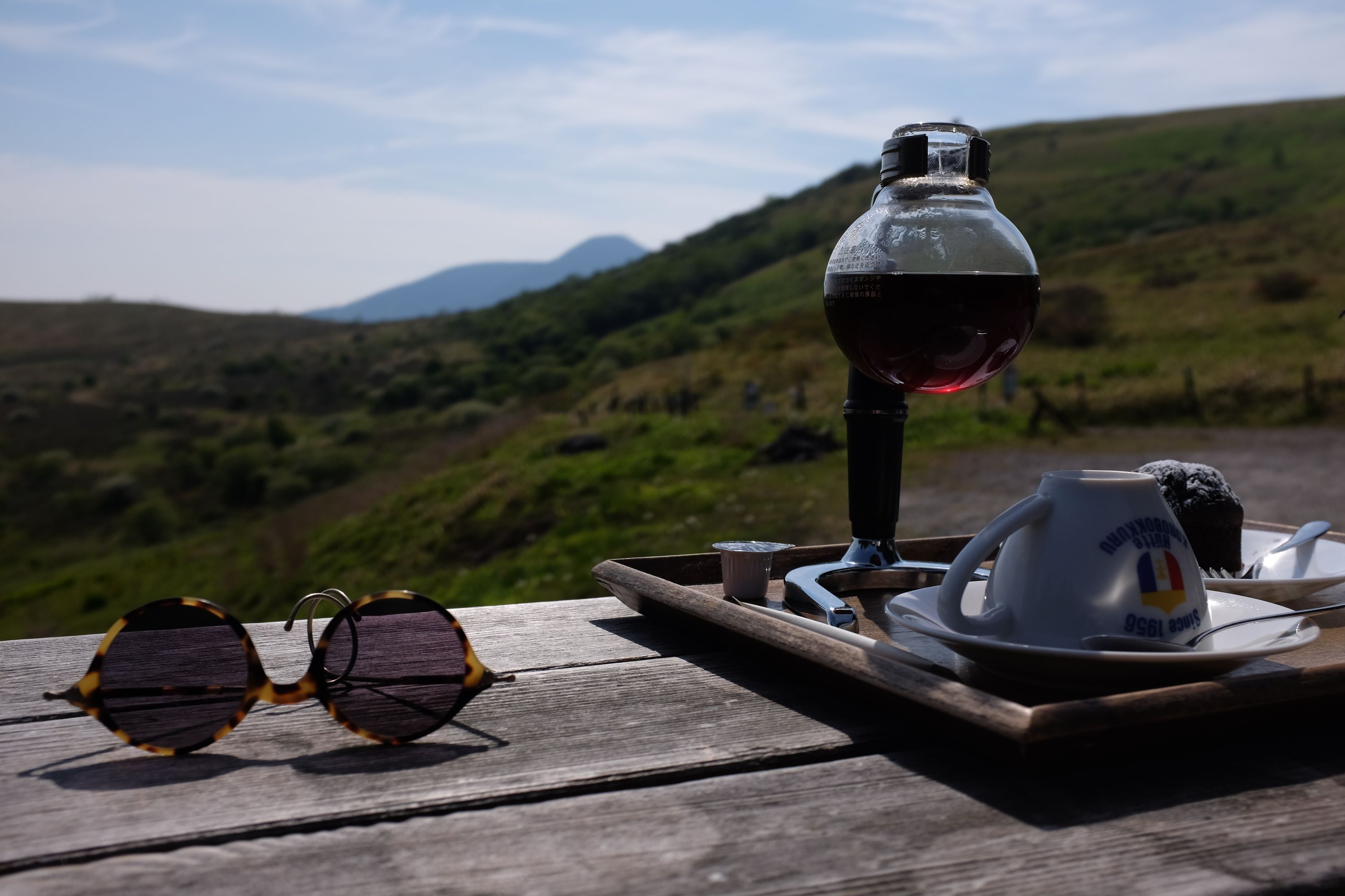 A pair of sunglasses and a siphon coffee pot on an outside table.