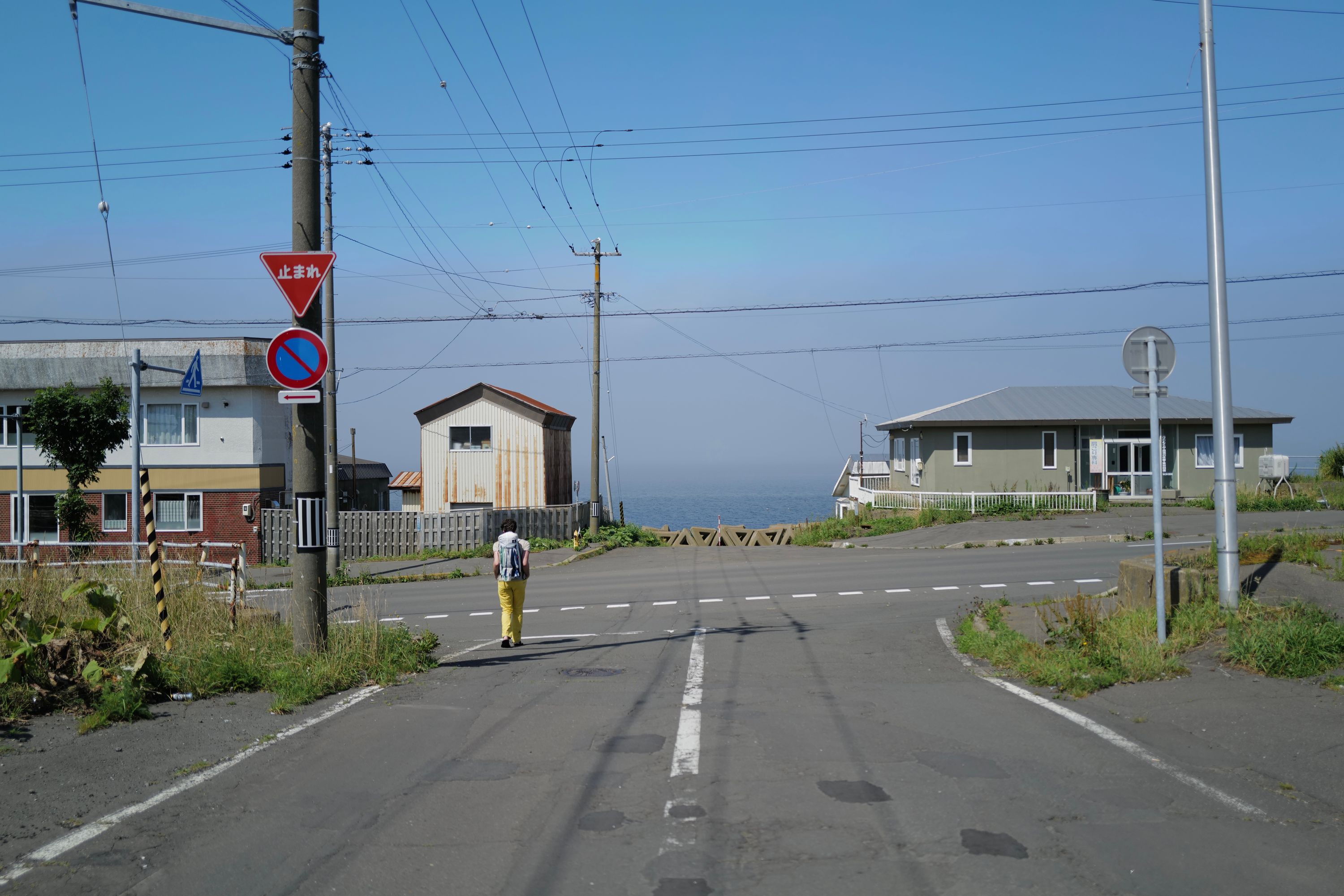A person stands on an empty street with the sea at its end.