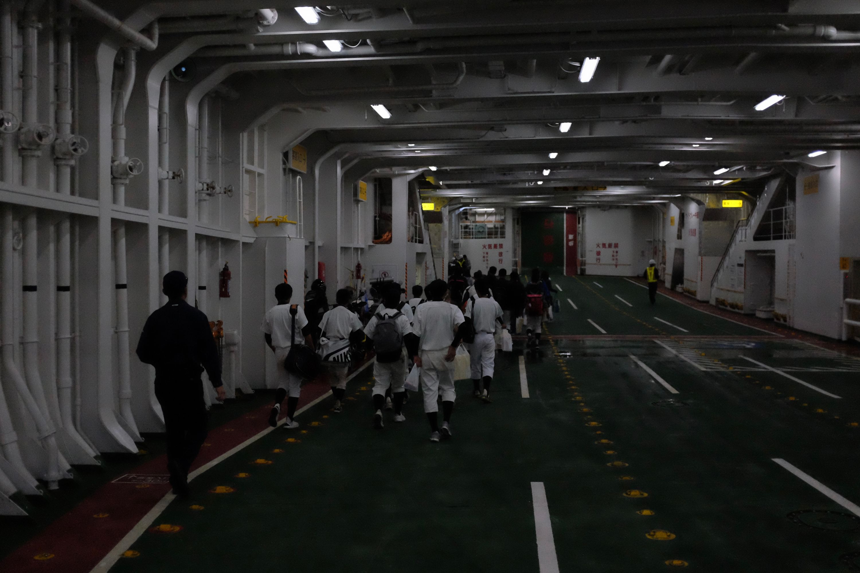 A group of boys in baseball uniforms walk through the car deck of the ferry.