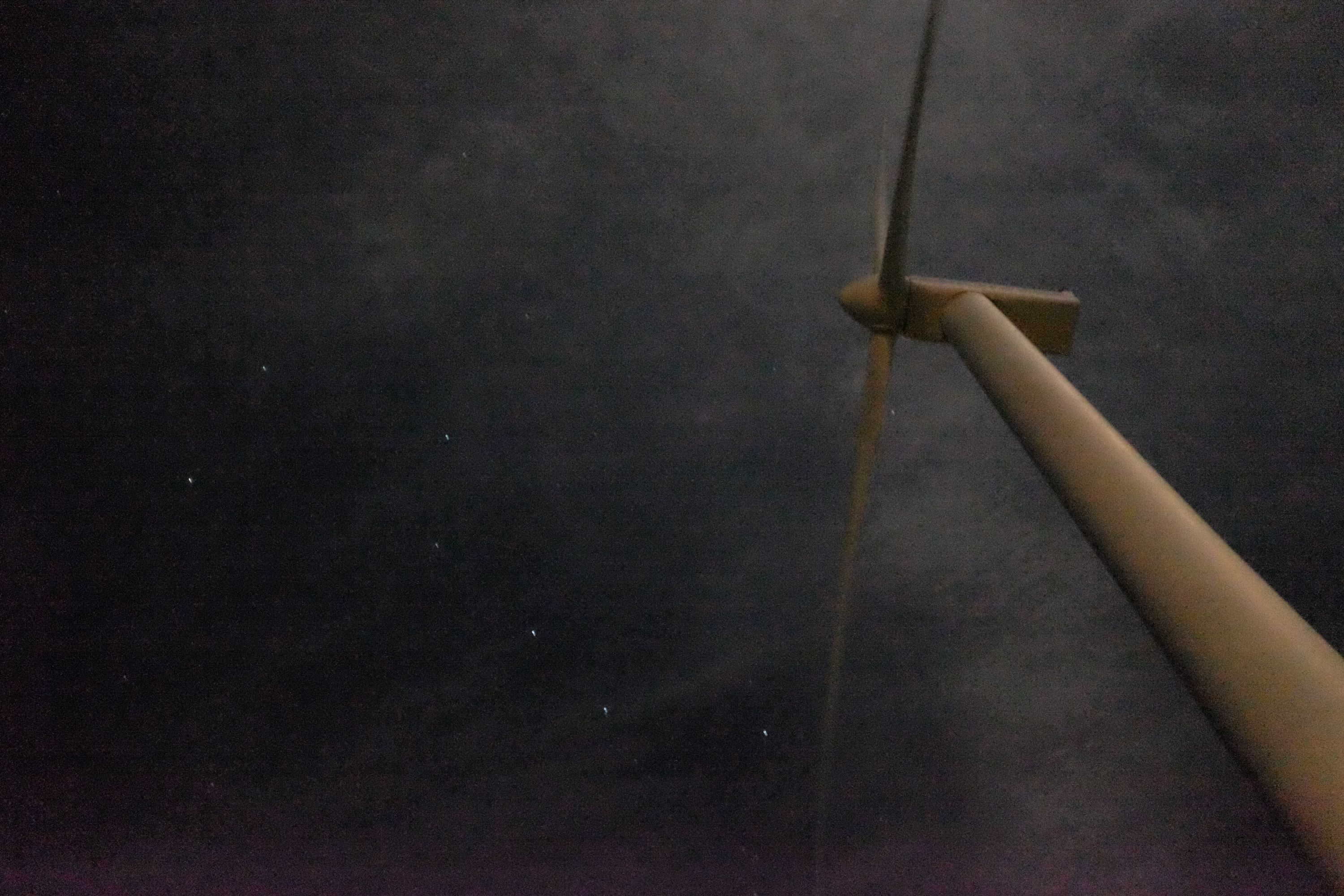 Looking up at a wind turbine at night, the constallation Ursa Major visible by its blades in the night sky.