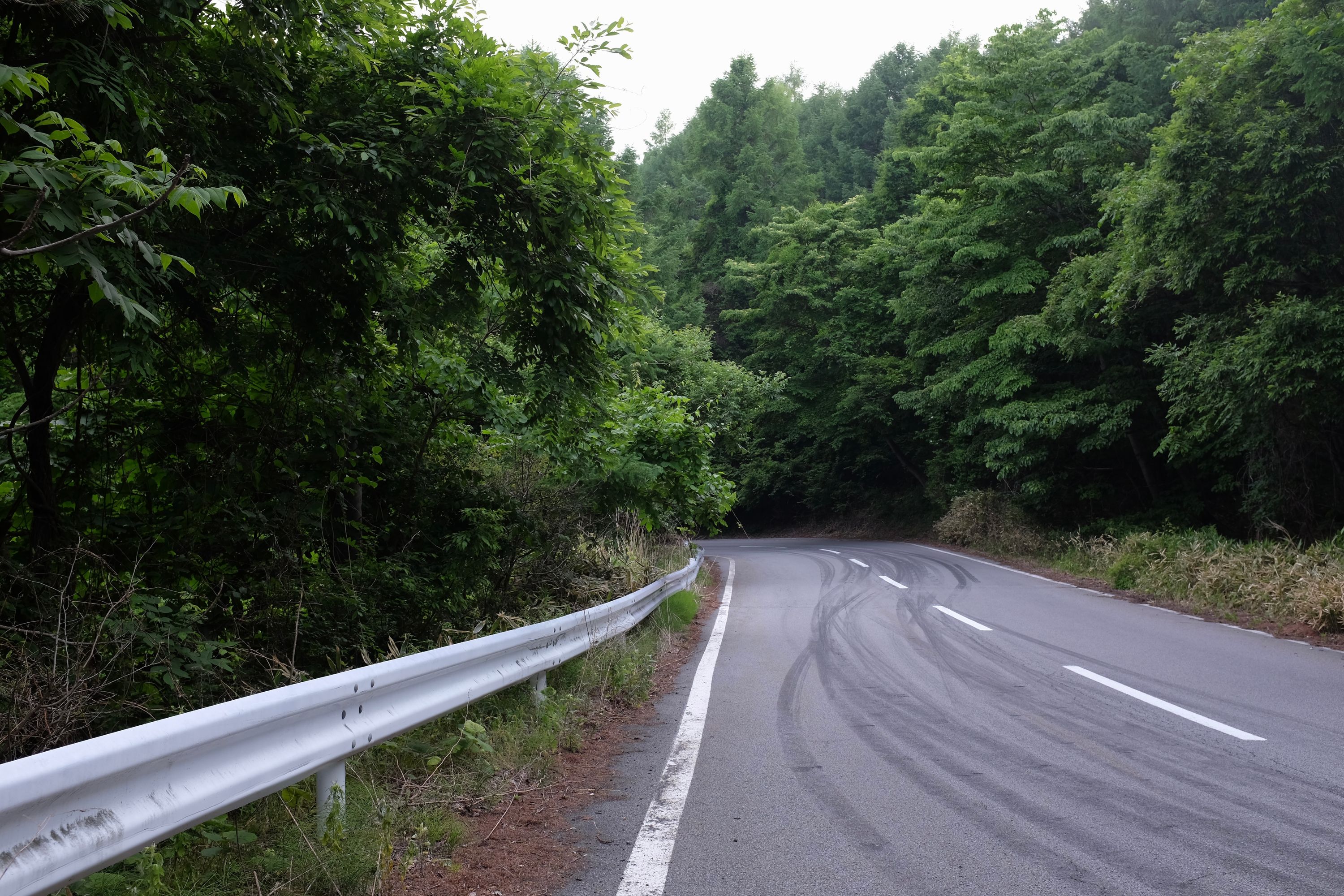 A mountain road shows tire marks indicating drifting-style car races.