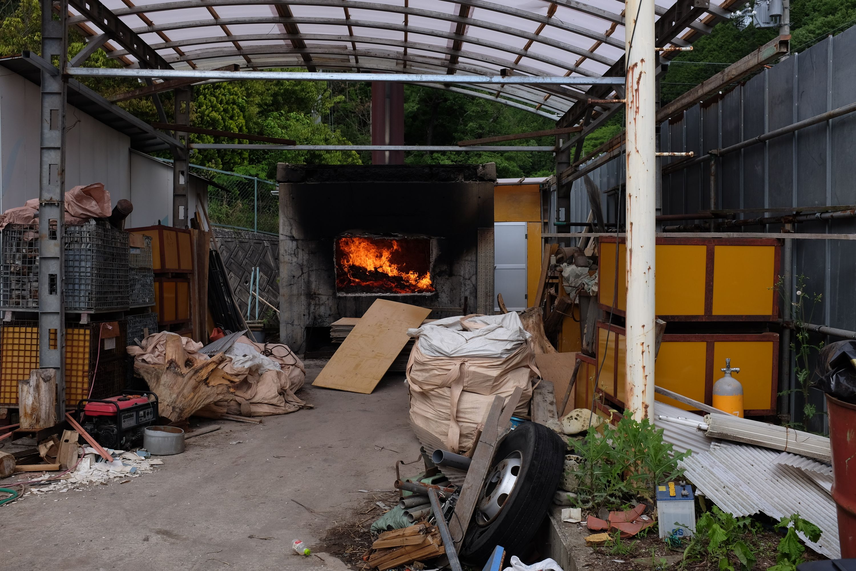 A huge trash fire burns in a furnace on a yard heaped with various piles of trash.