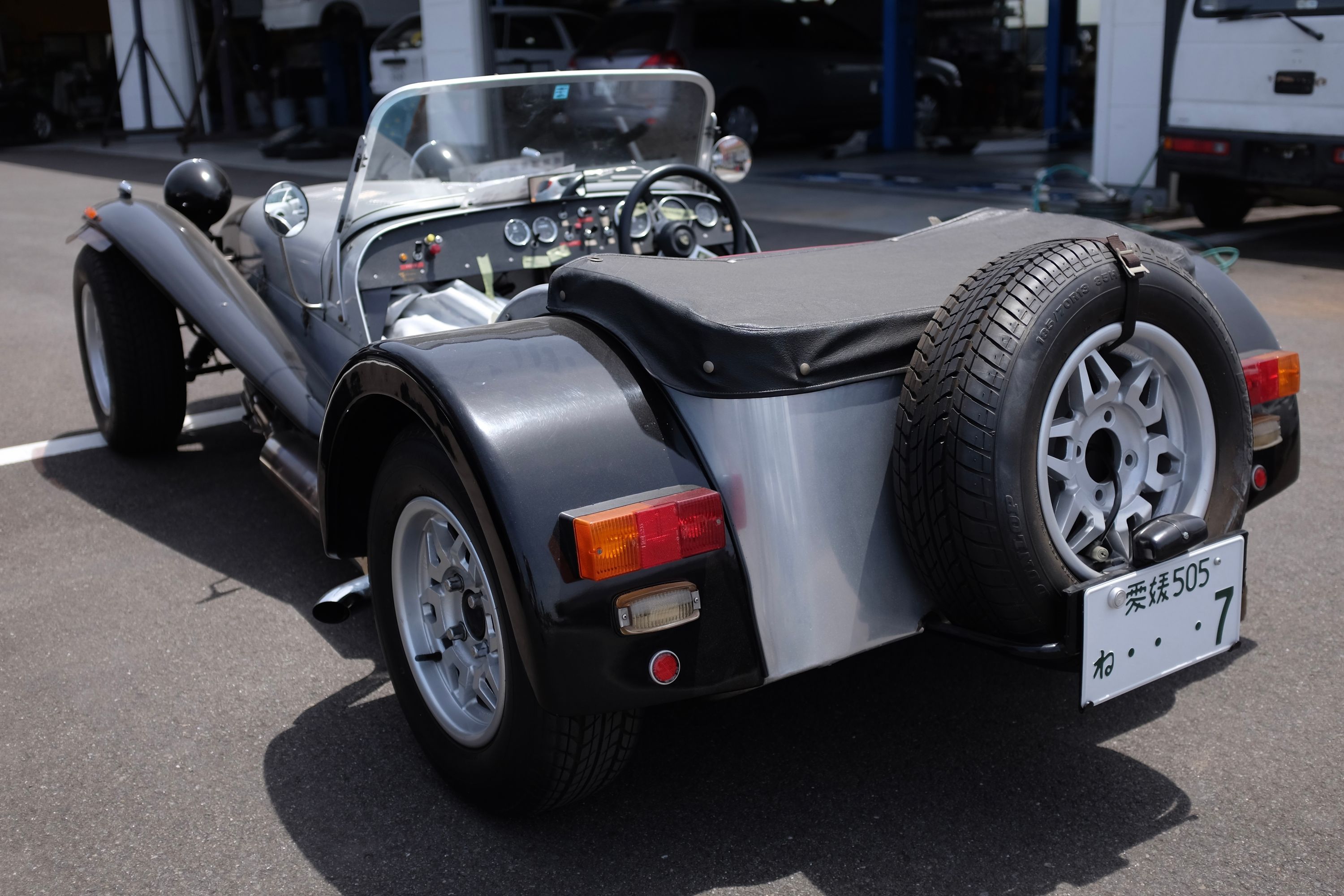 A silver and black Caterham Seven roadster whose Matsuyama license plate spells “わ.. .7”.