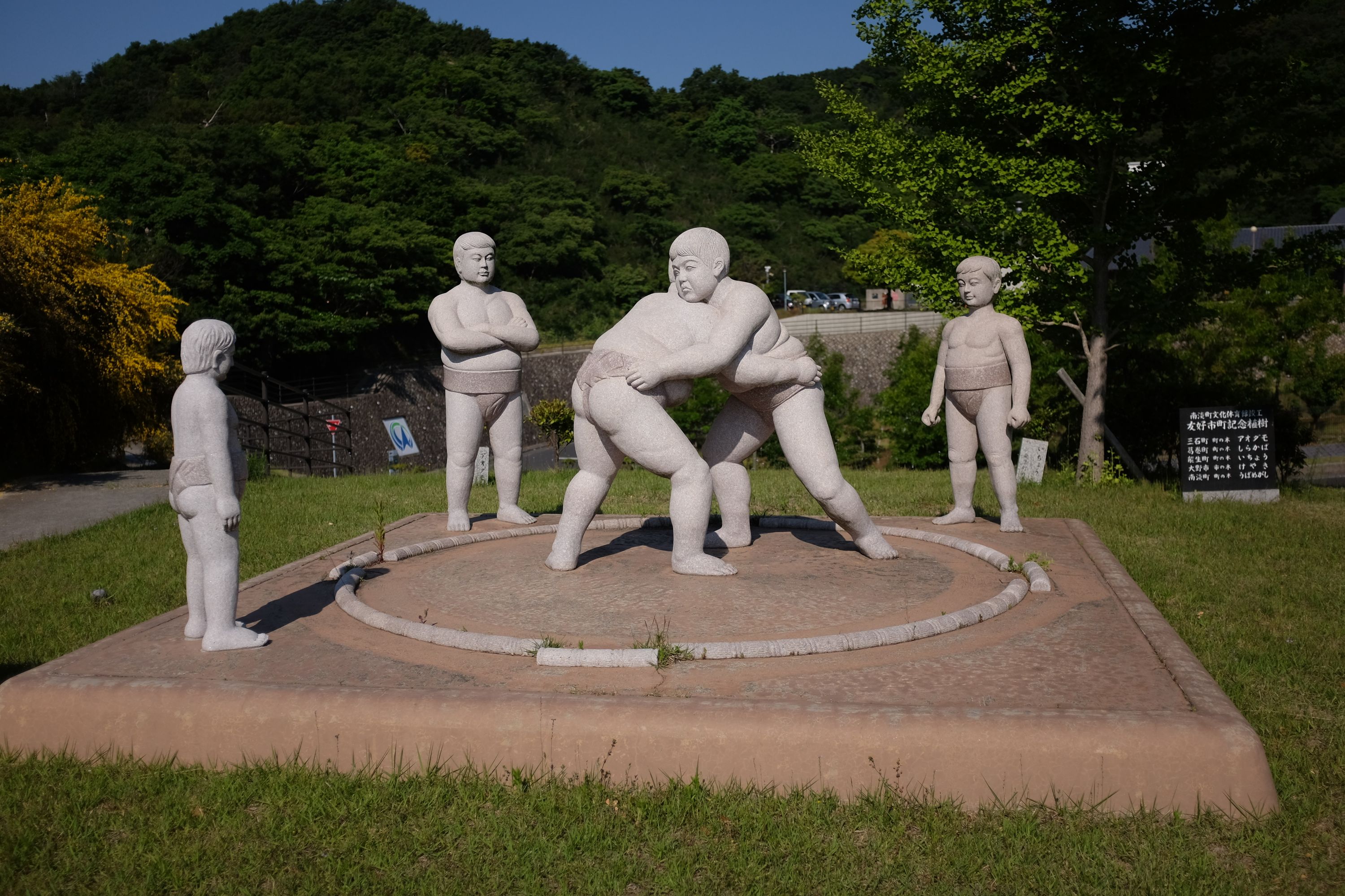 An open-air statue of five young sumo wrestlers: three watch while two wrestle.