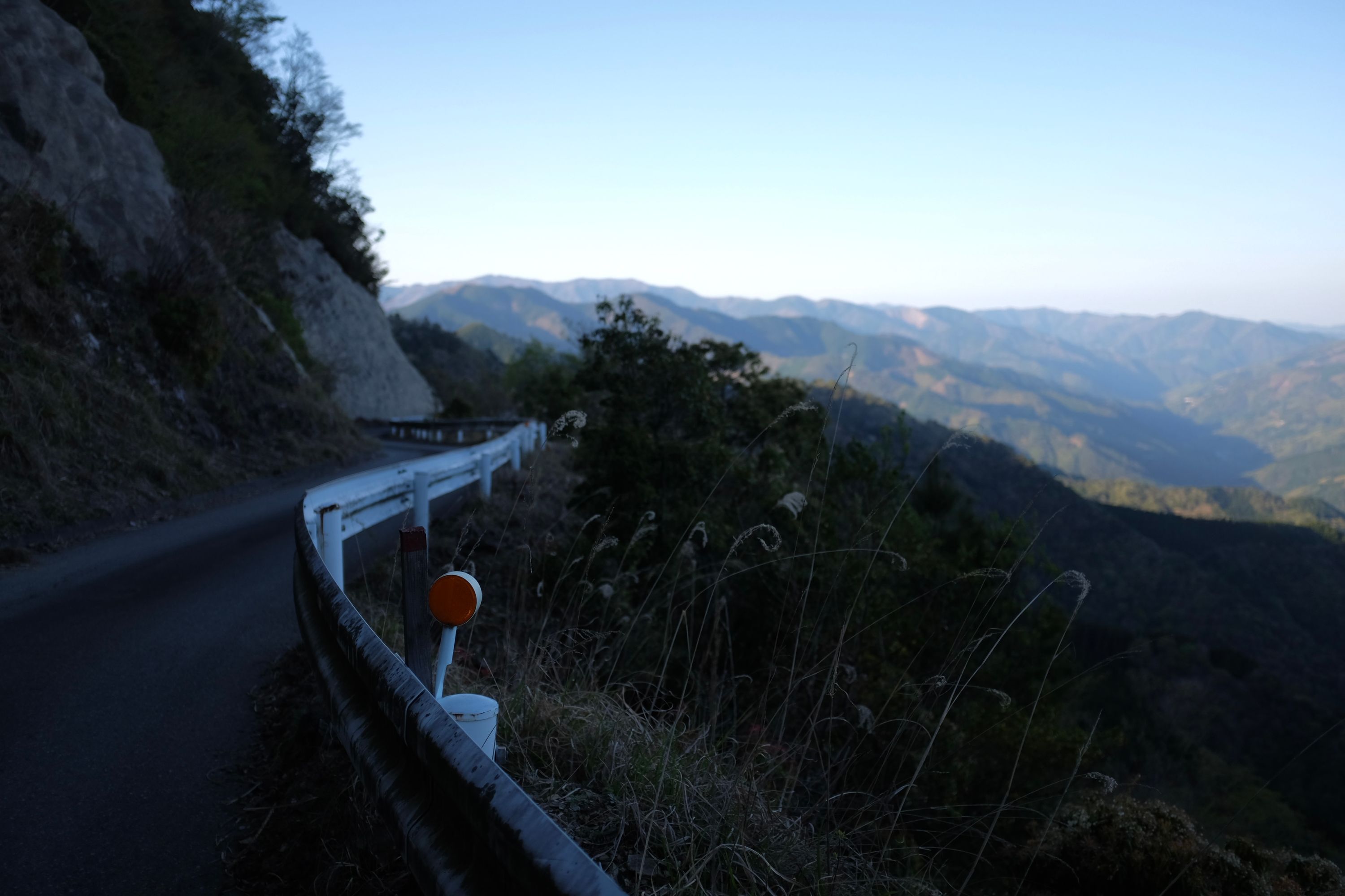 A narrow road goes over a mountain pass and reveals a landscape of forested hills.