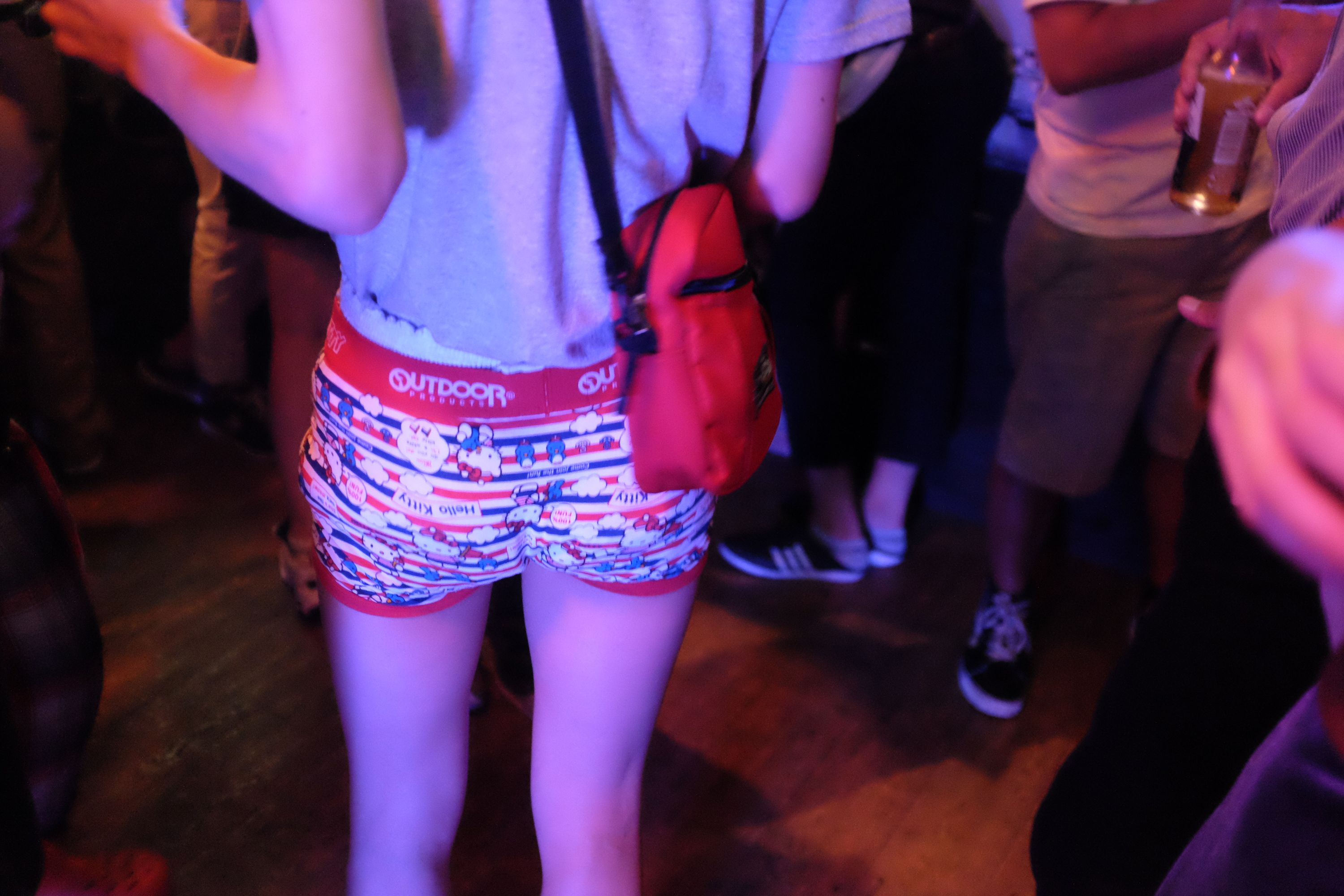 A person wears a pair of Hello Kitty shorts which look like boxer briefs in what looks like a crowded bar.