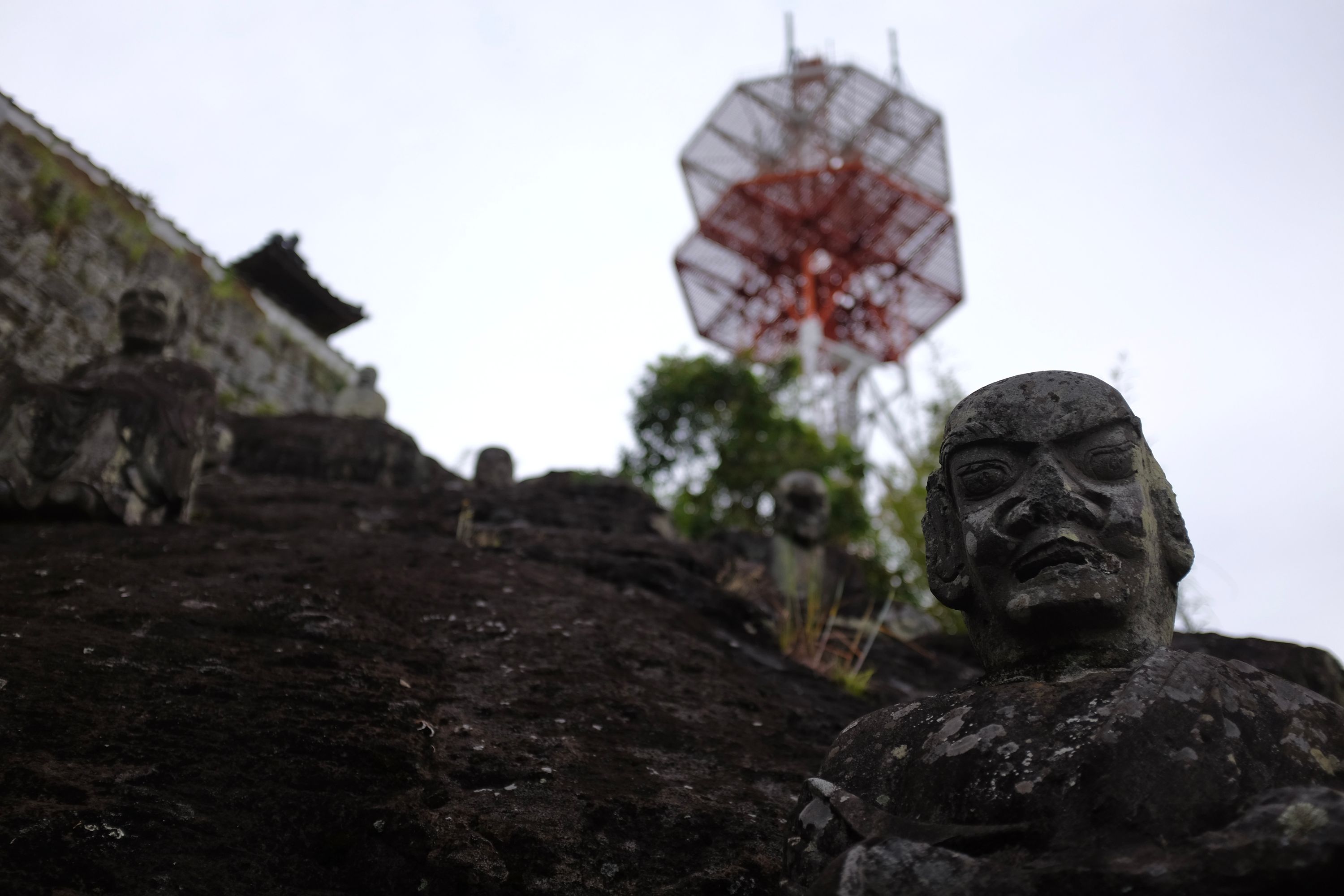 Statues of human heads carved from basalt on a hill, with two octogonal red antennas in the background.
