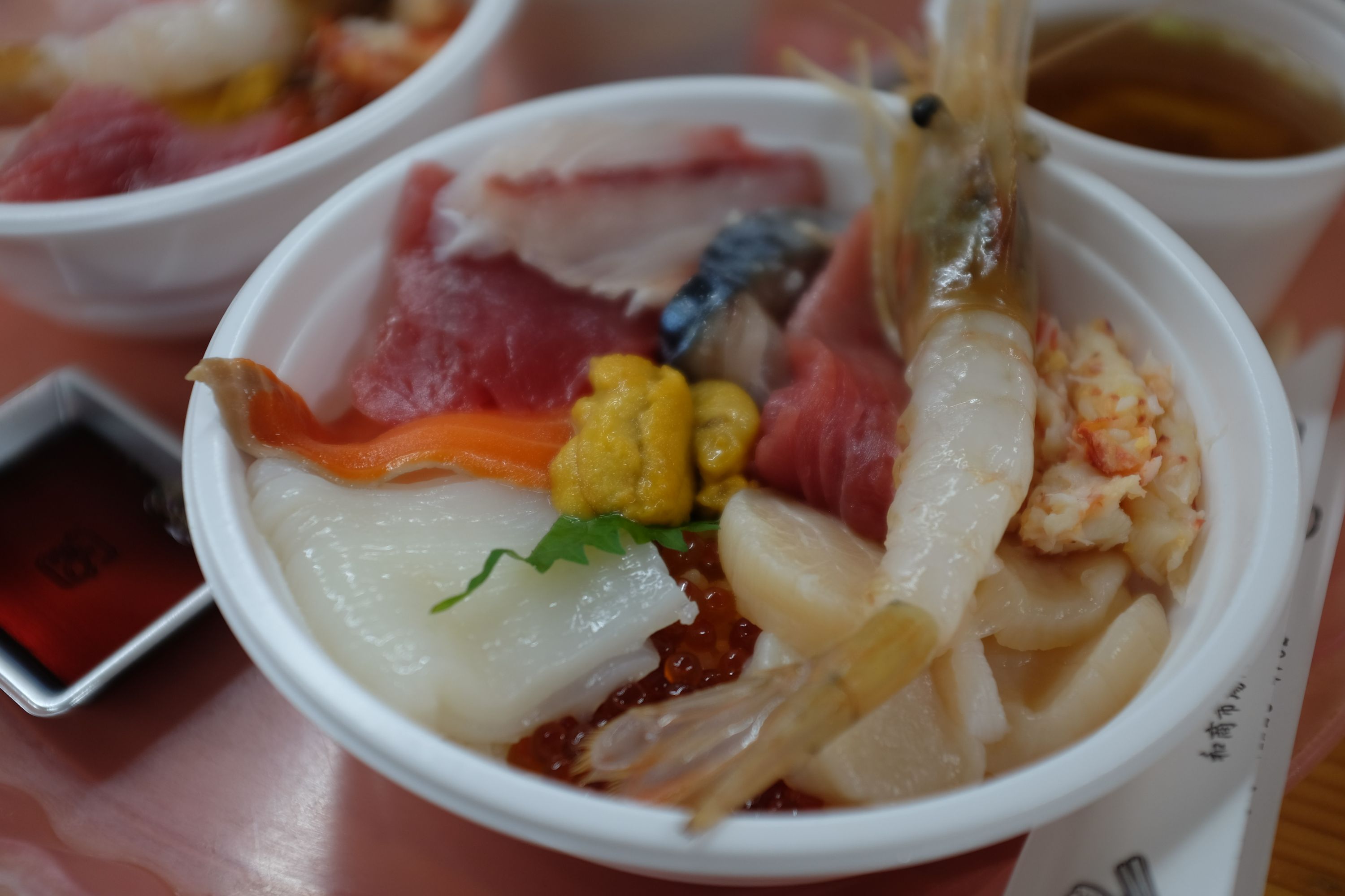 A lunch bowl of very colorful raw seafood: yellow sea urchin, pink shrimp, various pink and yellow fish, white squid, white-yellow crab.
