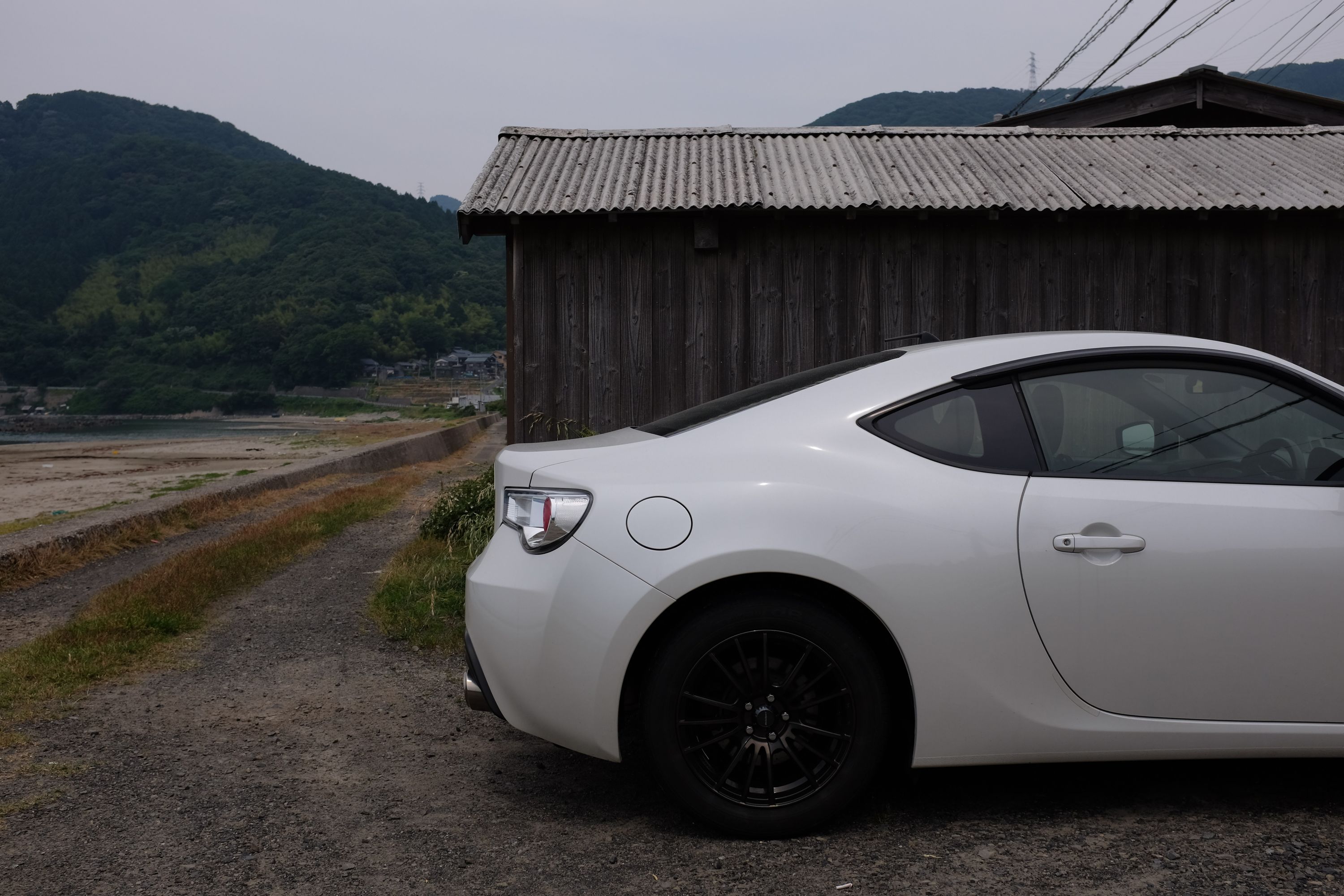 The rear of a white Toyota GT86 parked by a shed.