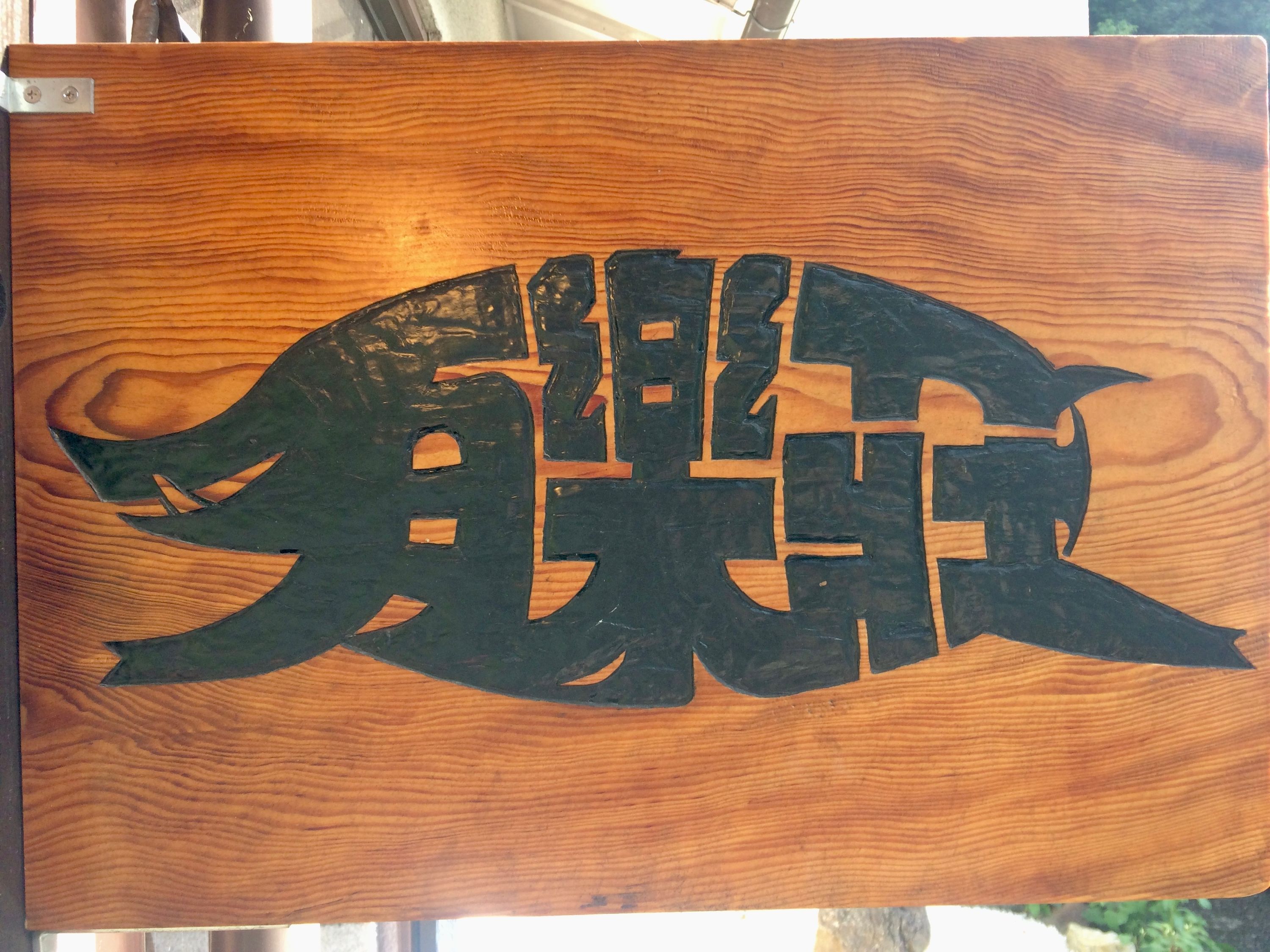 The calligraphic picture of a wild boar, made up of the characters 有楽荘, on a wooden board.